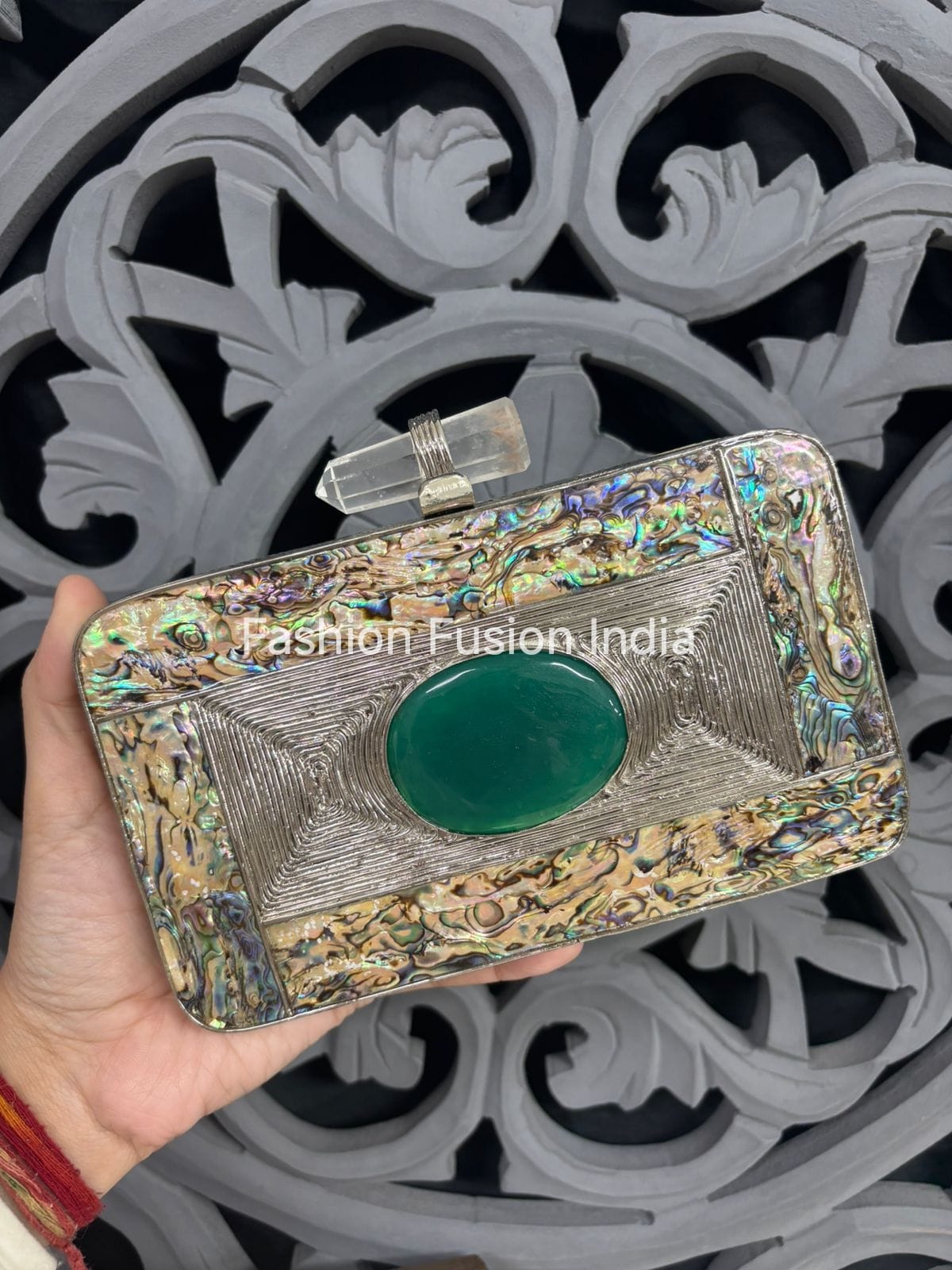 Decorative clutch held by a hand with intricate design in the background