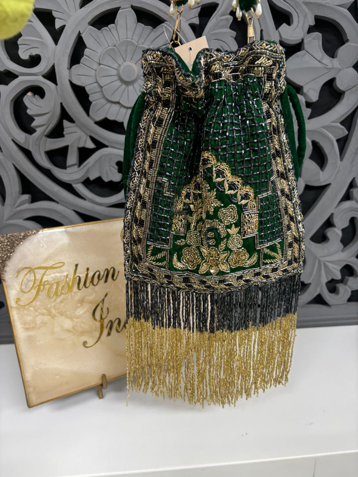 Green and gold beaded handbag with fringe on a decorative background