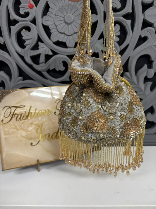 Decorative handbag with gold and silver embellishments on a white surface with a decorative background.