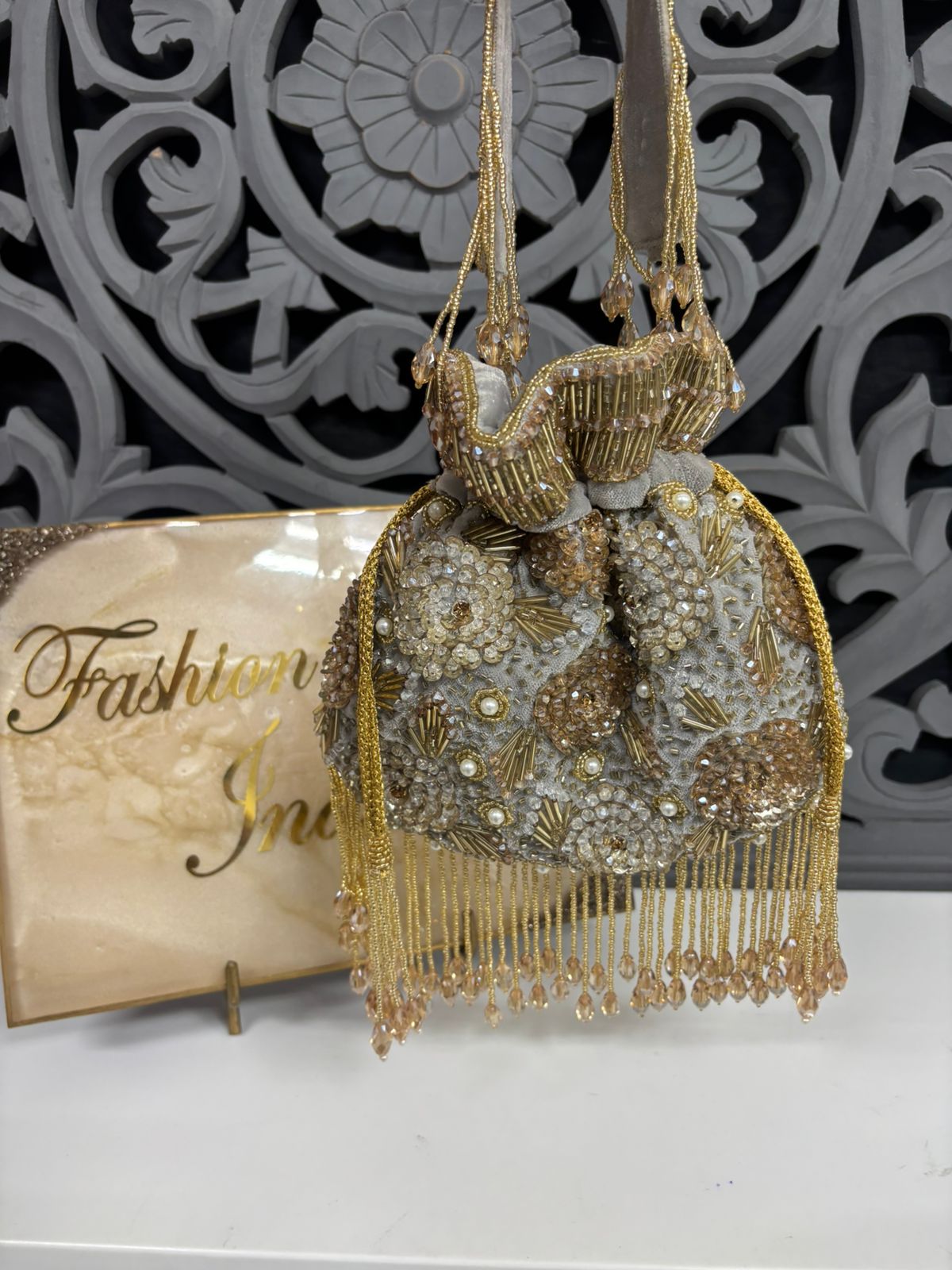 Decorative handbag with gold fringe and beads on a white surface with 'Fashion India' sign.