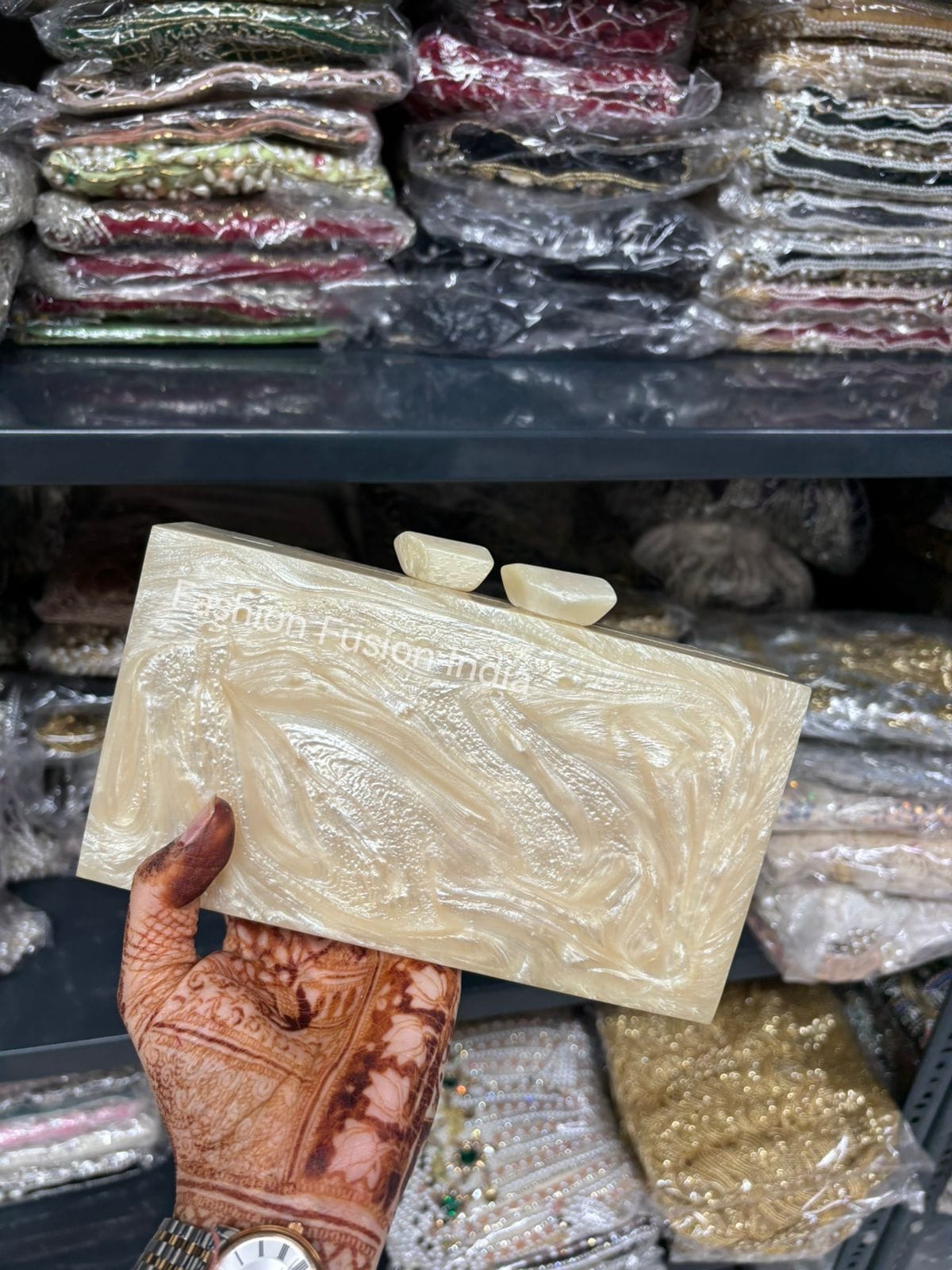 Hand holding a decorative item with 'Indian Fusion India' branding in front of shelves with various items.