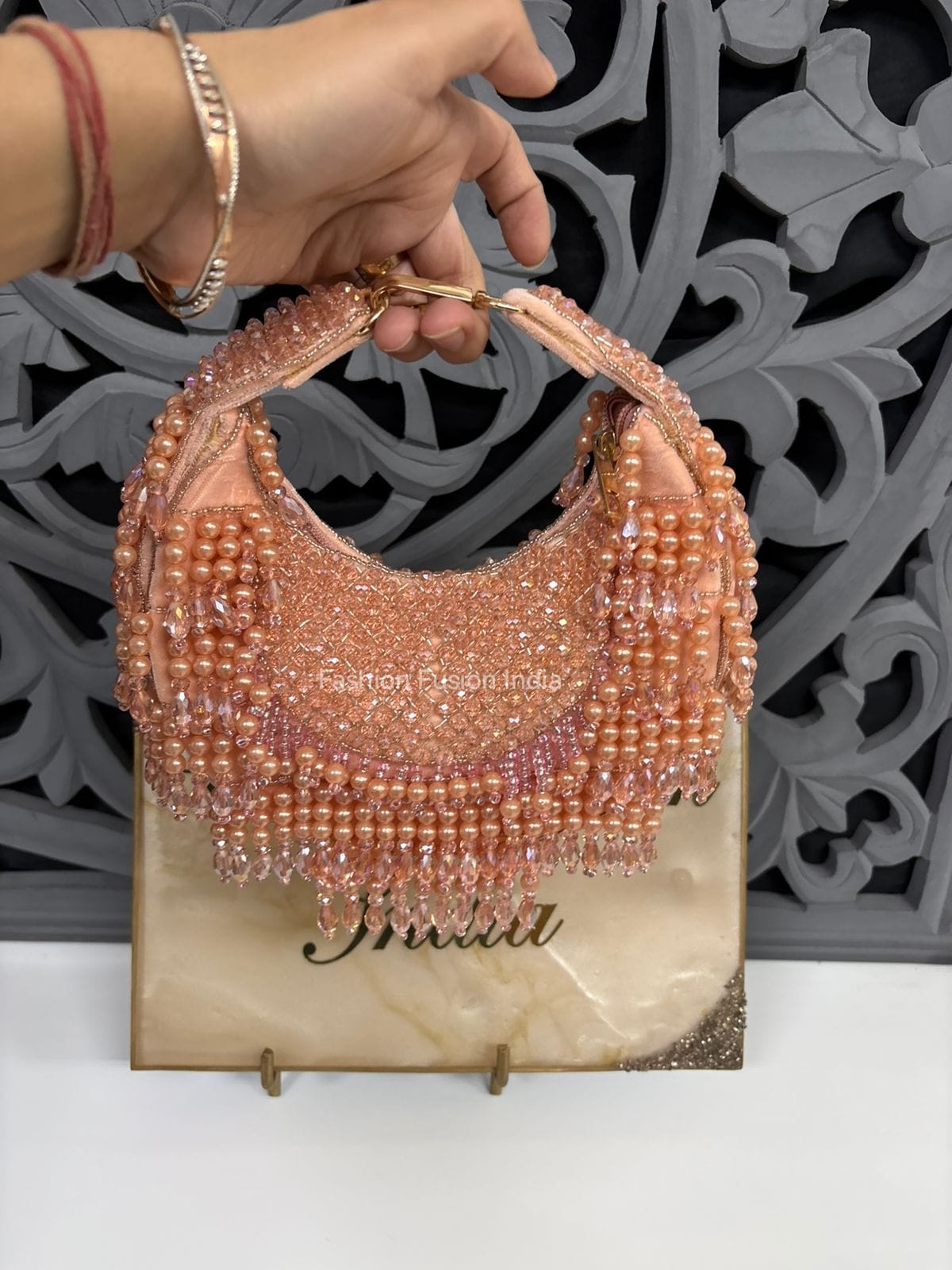 Hand holding a beaded handbag with intricate design on a decorative background