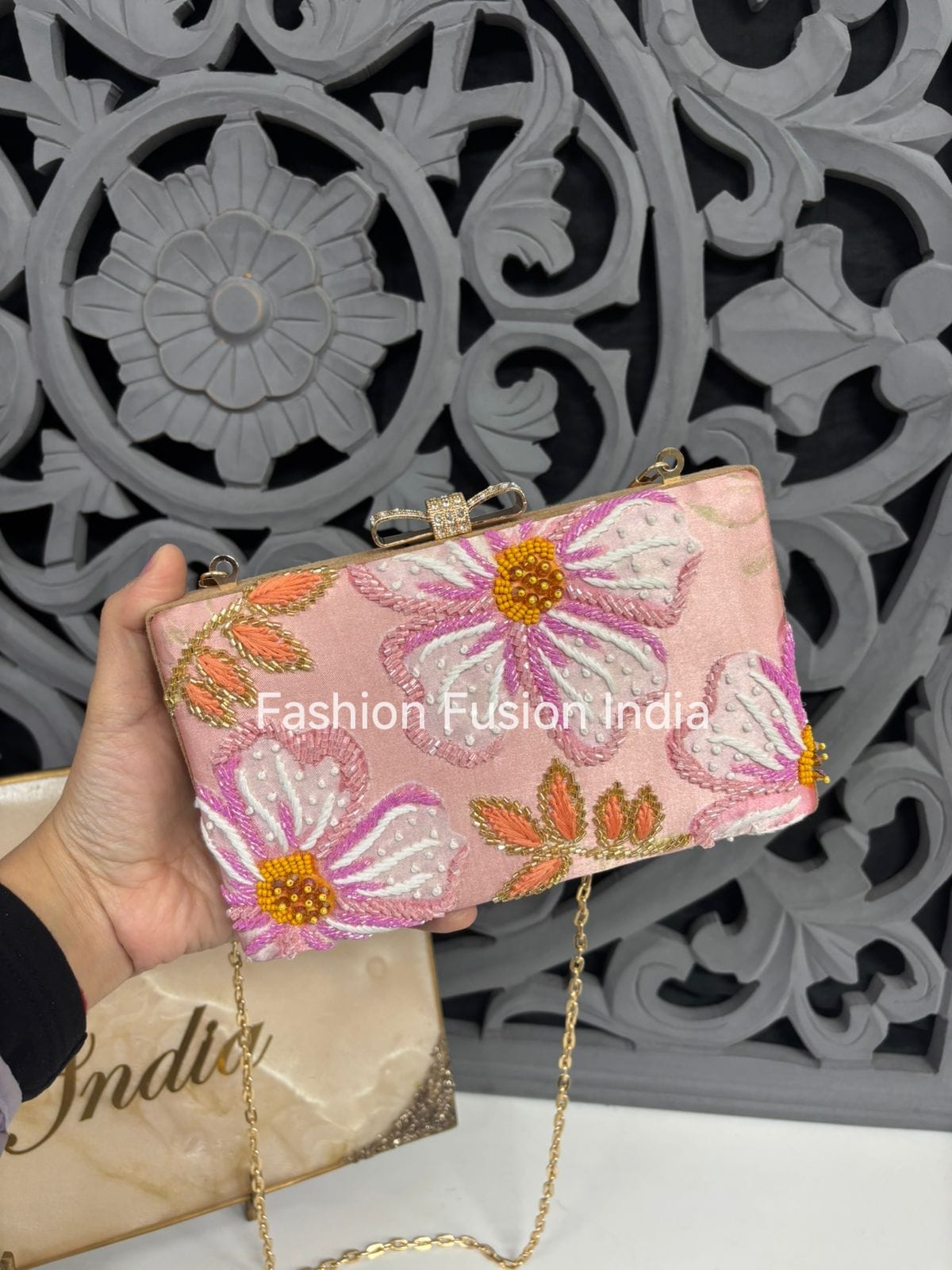 Handheld pink clutch with floral embroidery against a decorative wall.