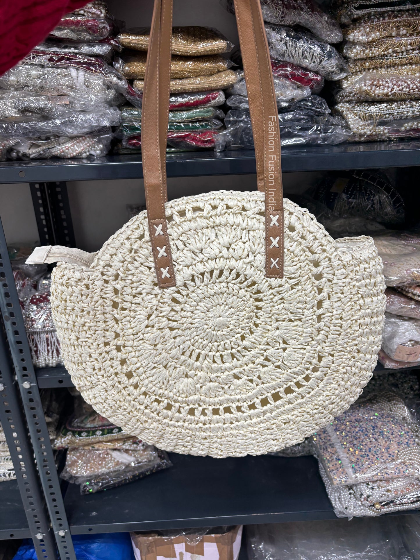 Round woven beige bag with brown straps on a shelf with other bags in the background
