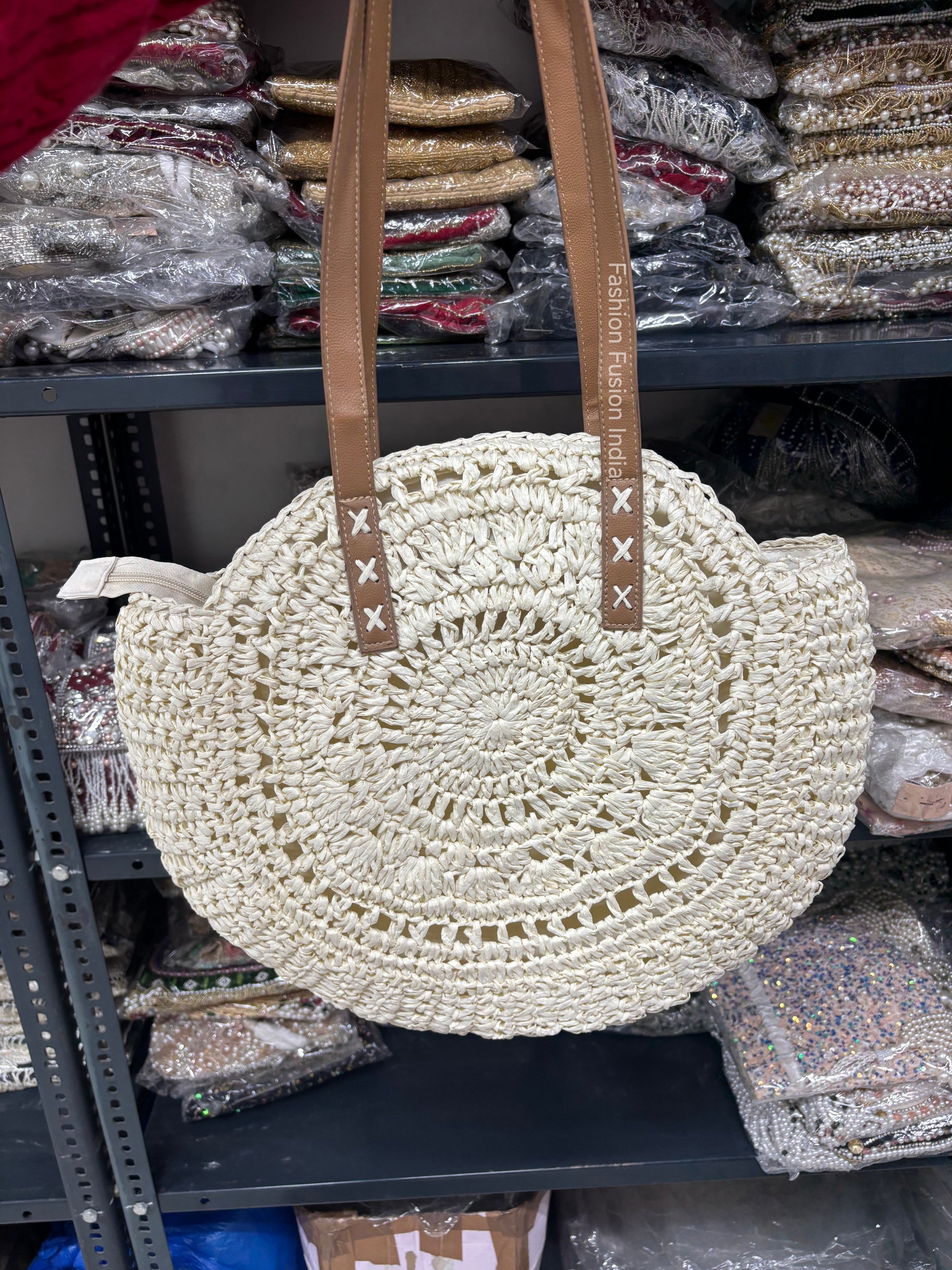 Round woven beige bag with brown straps on a shelf with other bags in the background