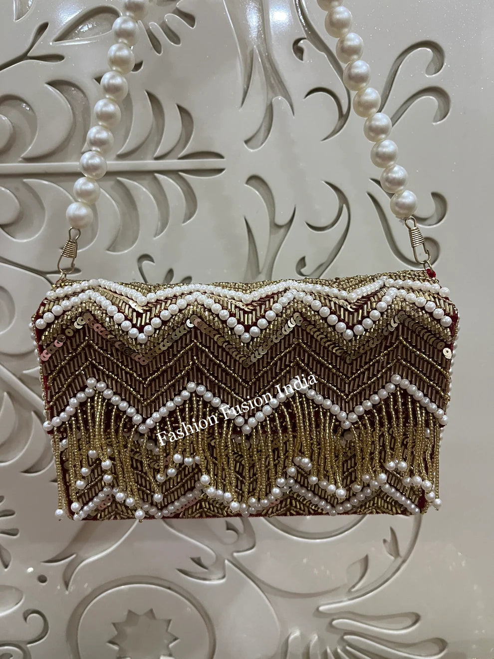 Decorative clutch bag with chevron pattern and pearl embellishments on a textured white background.