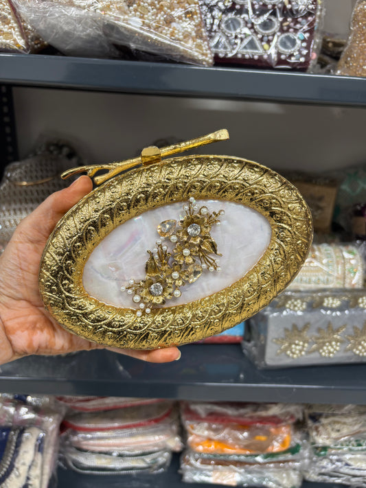 Gold decorative plate with a brooch held by a hand, with more decorative items in the background.