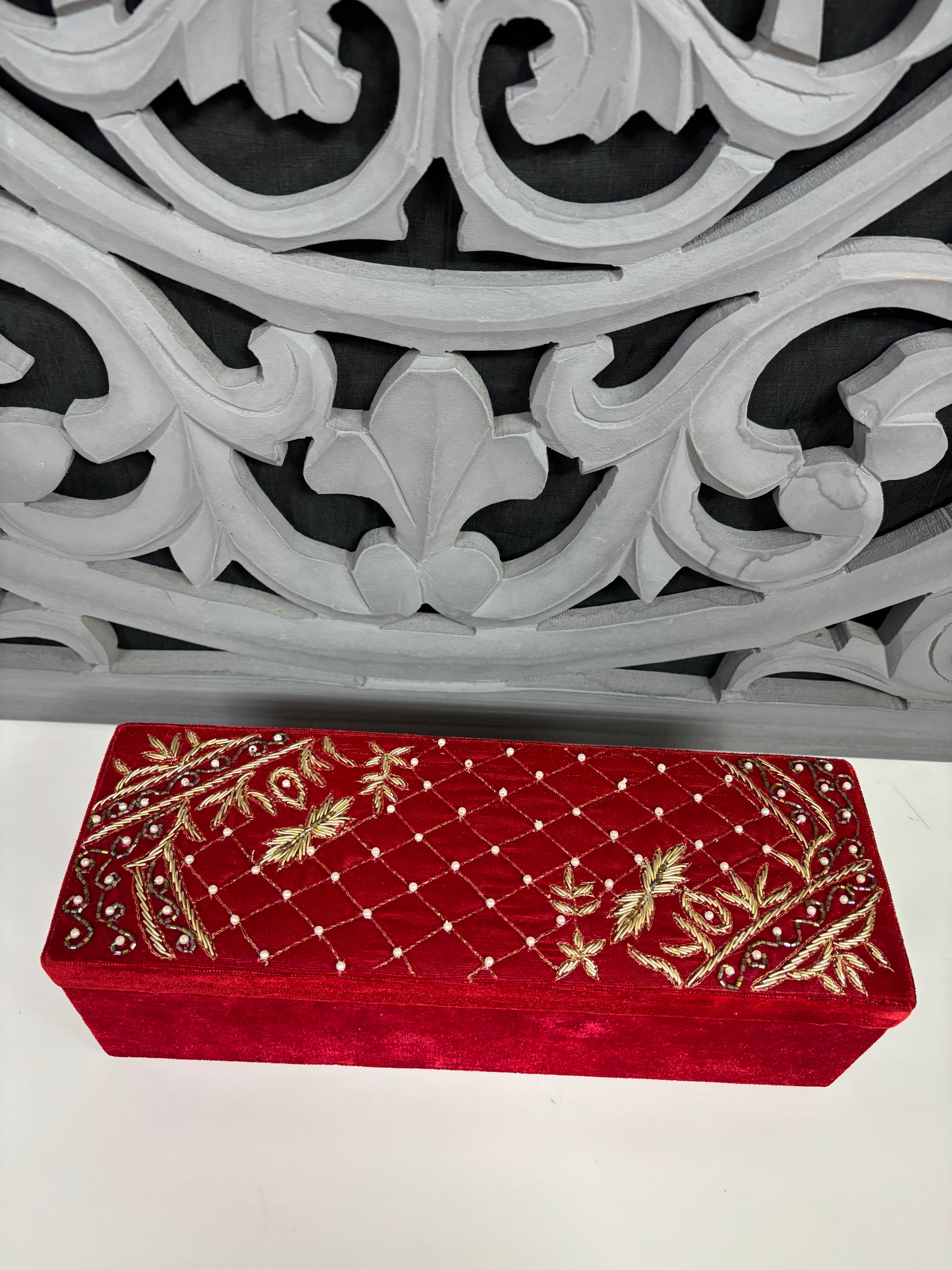Red embroidered box on a white surface with an ornate gray metal object in the background