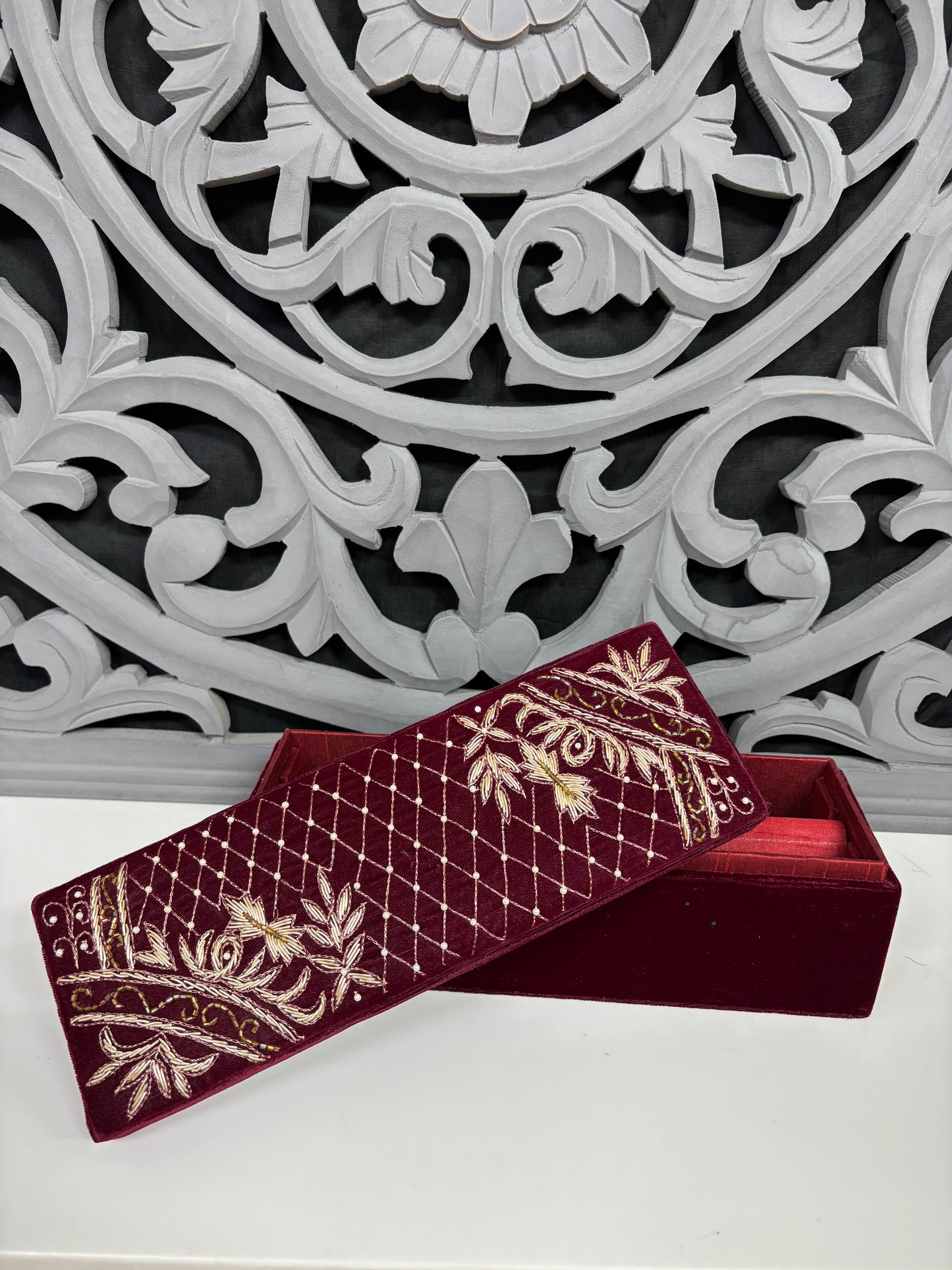 Decorative maroon box with gold embroidery against an ornate white and gray background