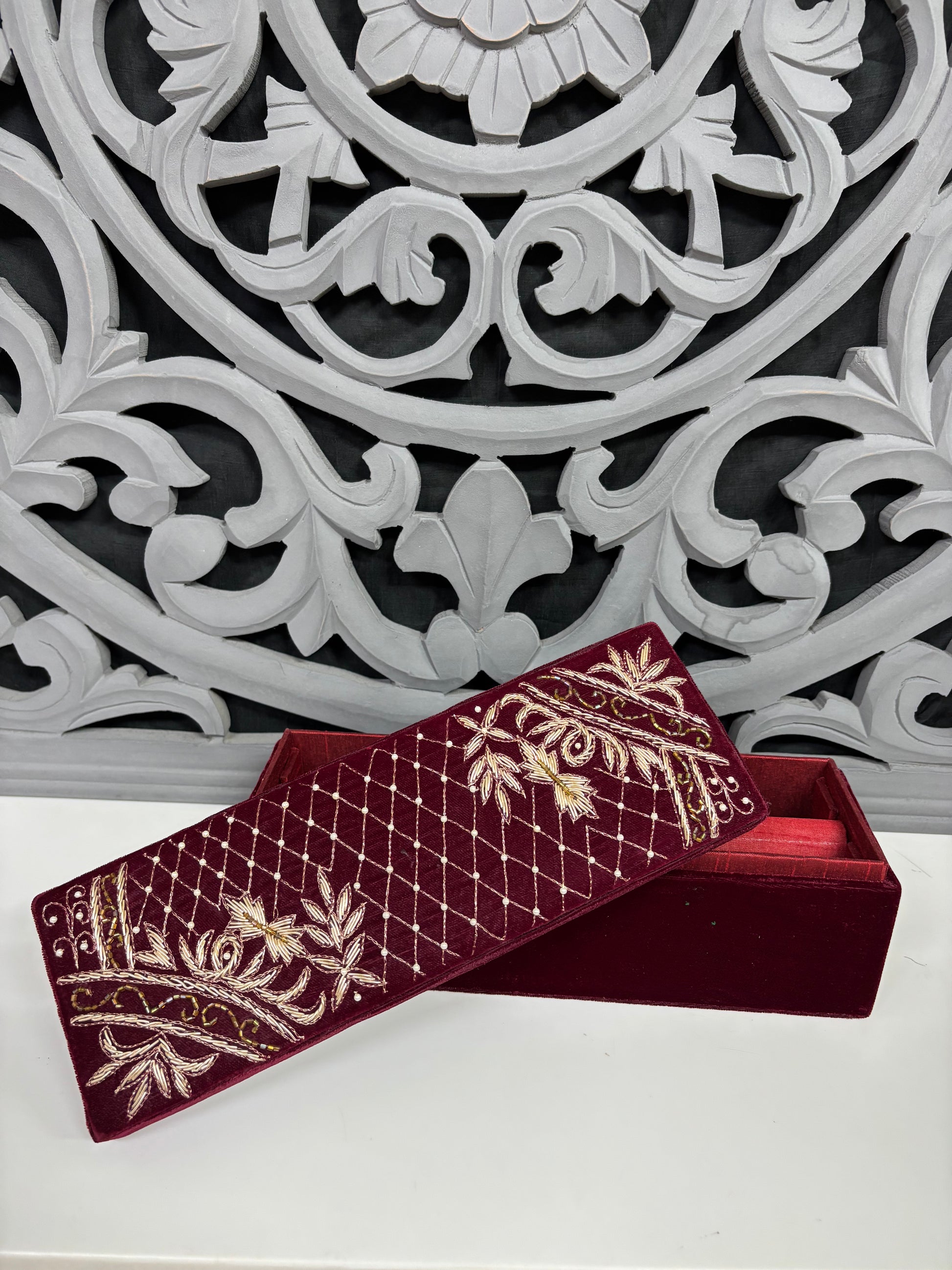 Decorative maroon box with gold embroidery against an ornate white and gray background