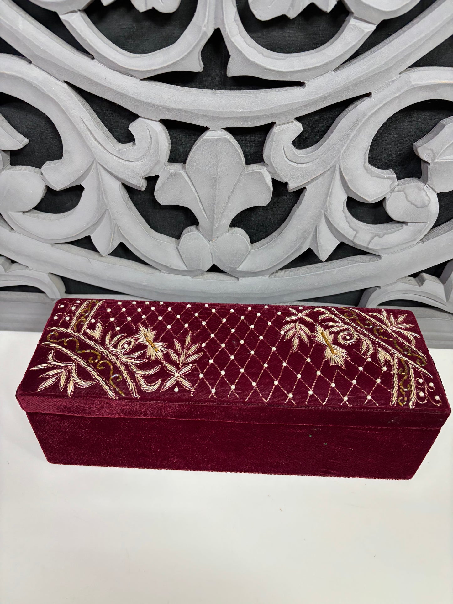 Maroon embroidered box with gold patterns on a decorative white lattice background