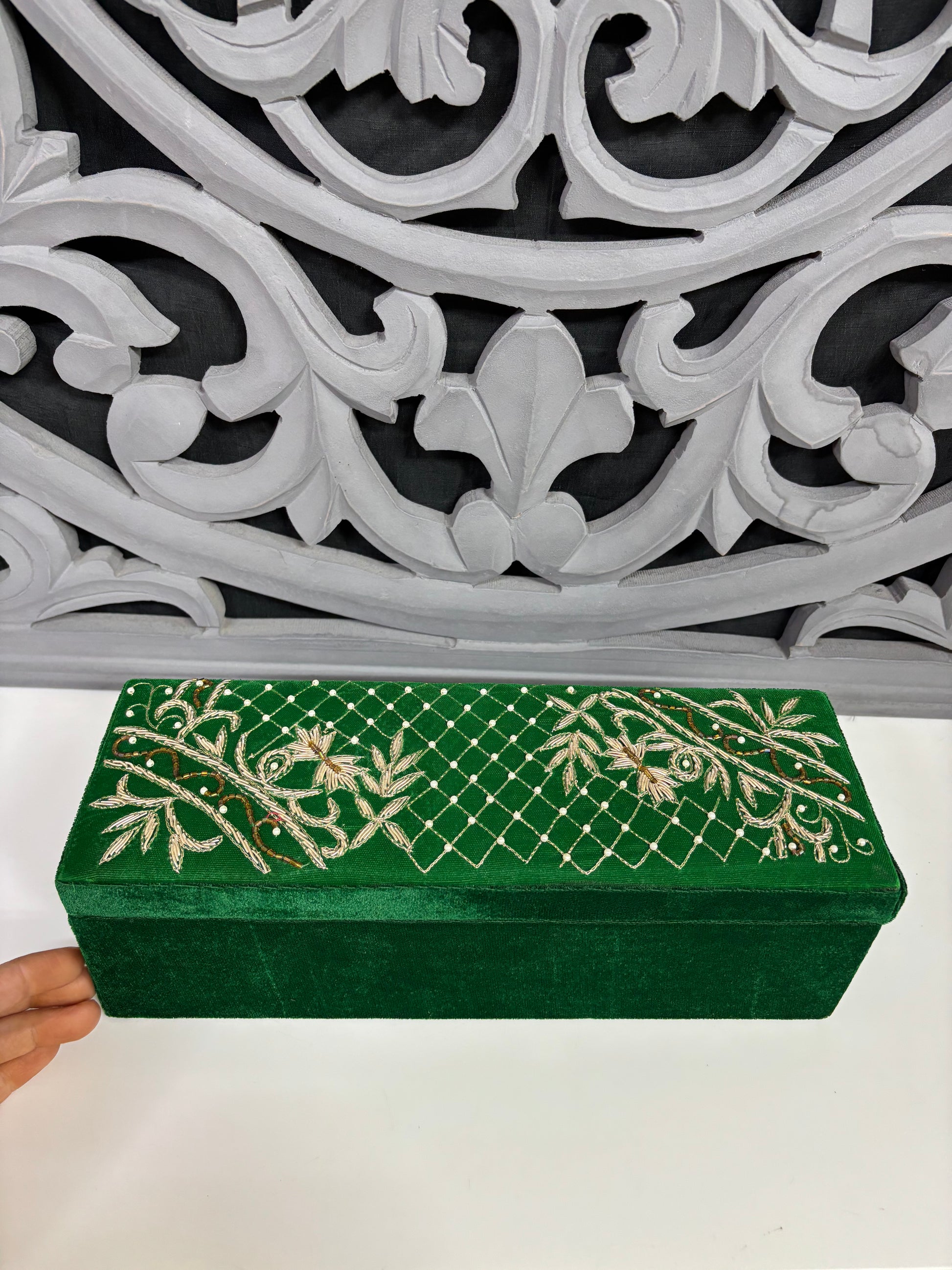 Green box with gold floral patterns held in front of decorative white and gray wall.