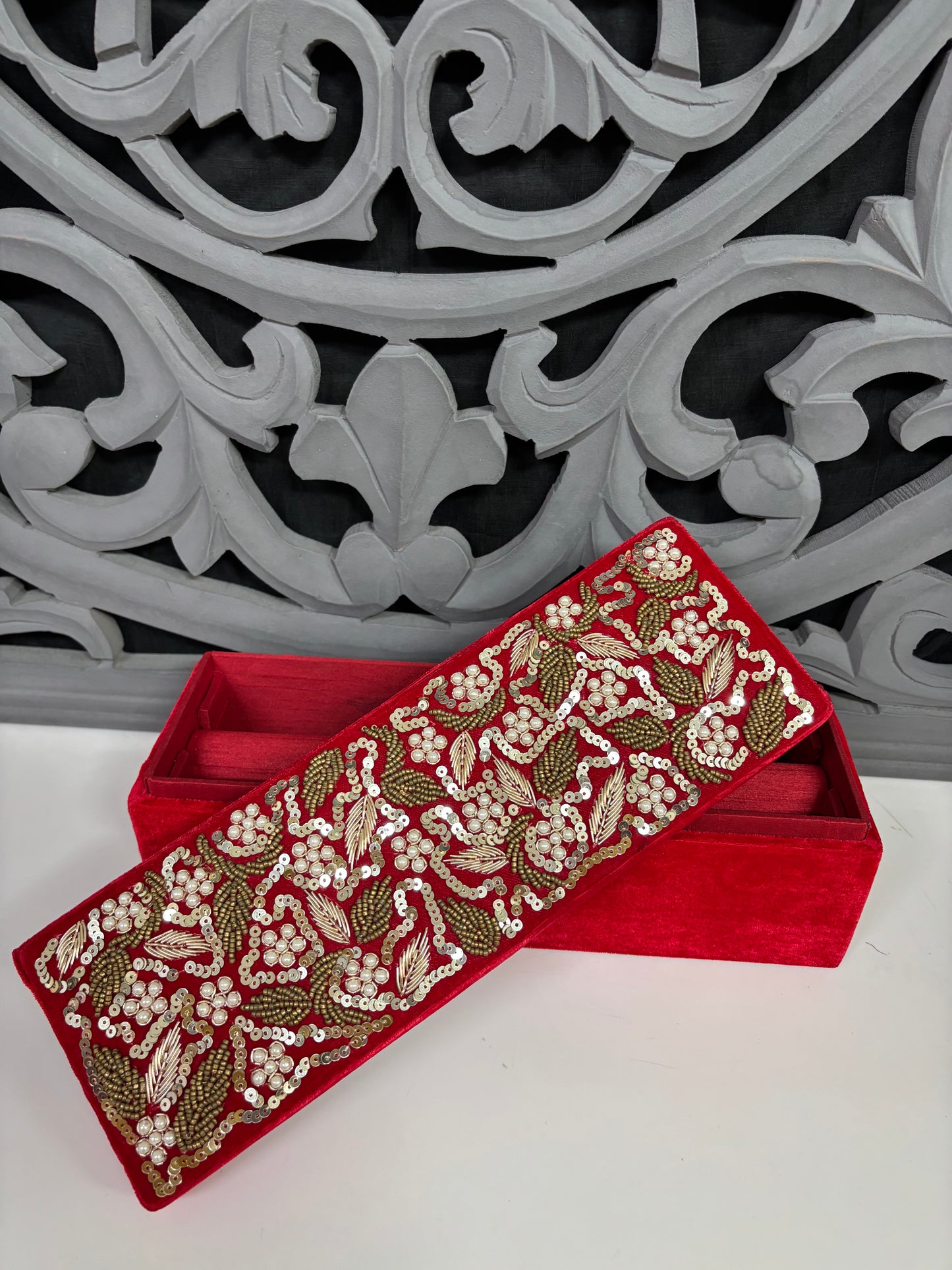 Decorative red box with gold and white floral embroidery against a gray decorative background