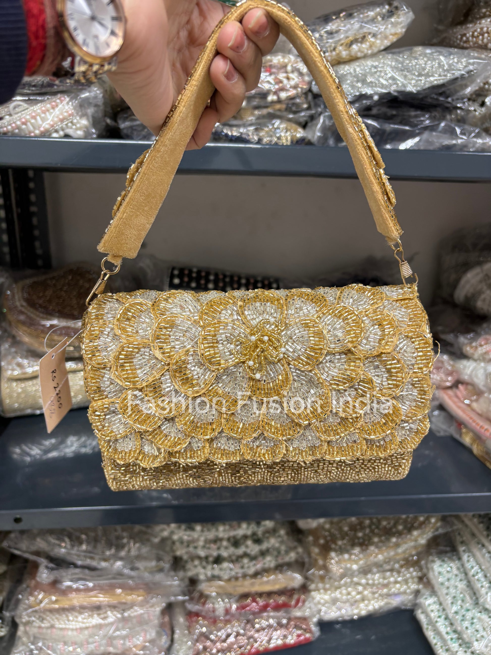 Gold beaded handbag held by a person with a blurred background of similar bags.