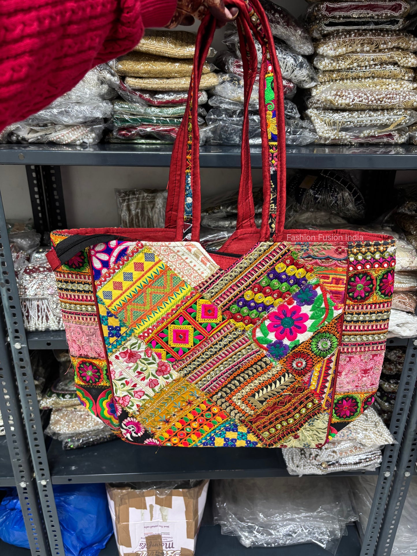 Colorful embroidered handbag held by a person with shelves of fabric in the background