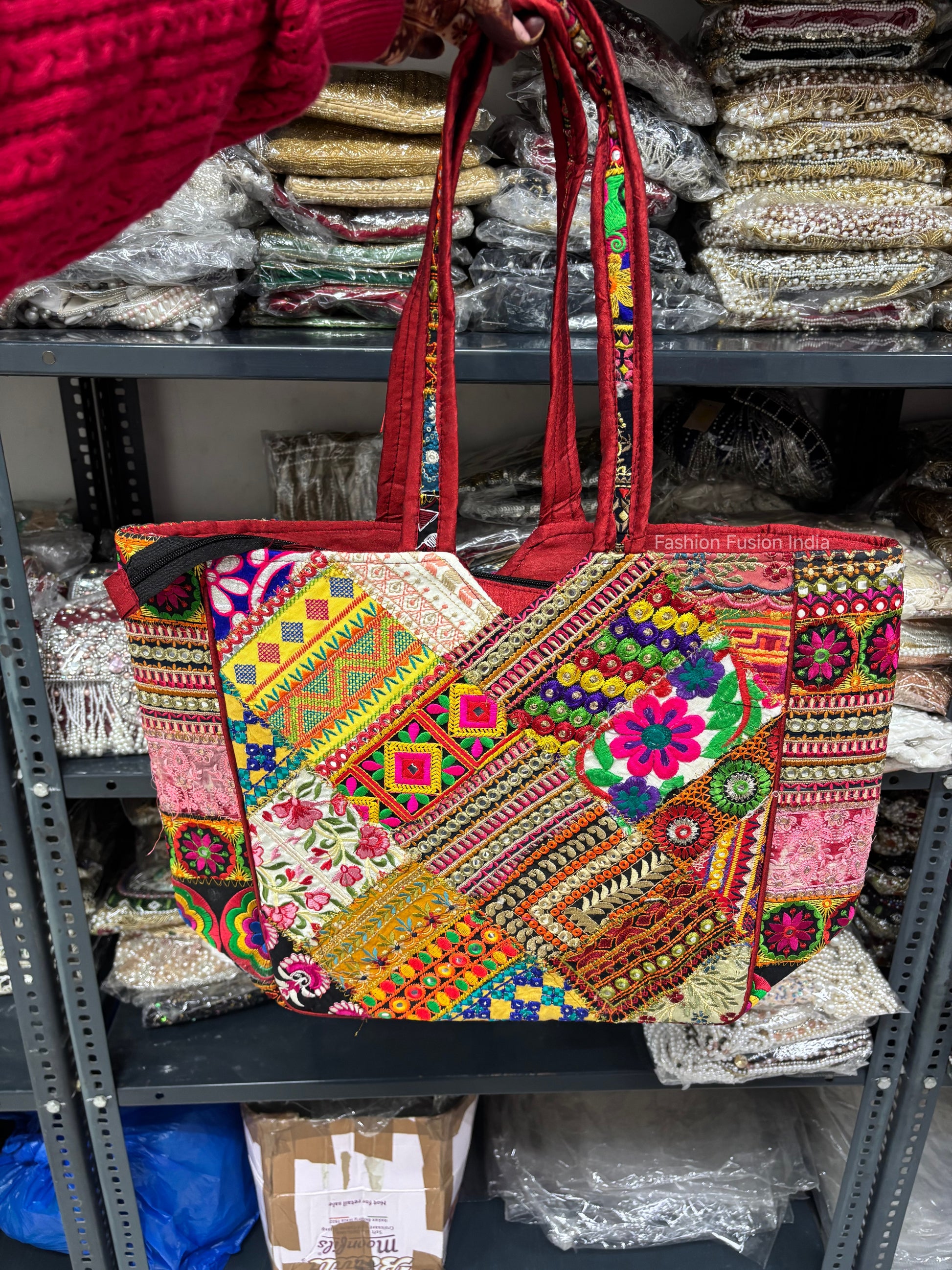 Colorful embroidered handbag held by a person with shelves of fabric in the background
