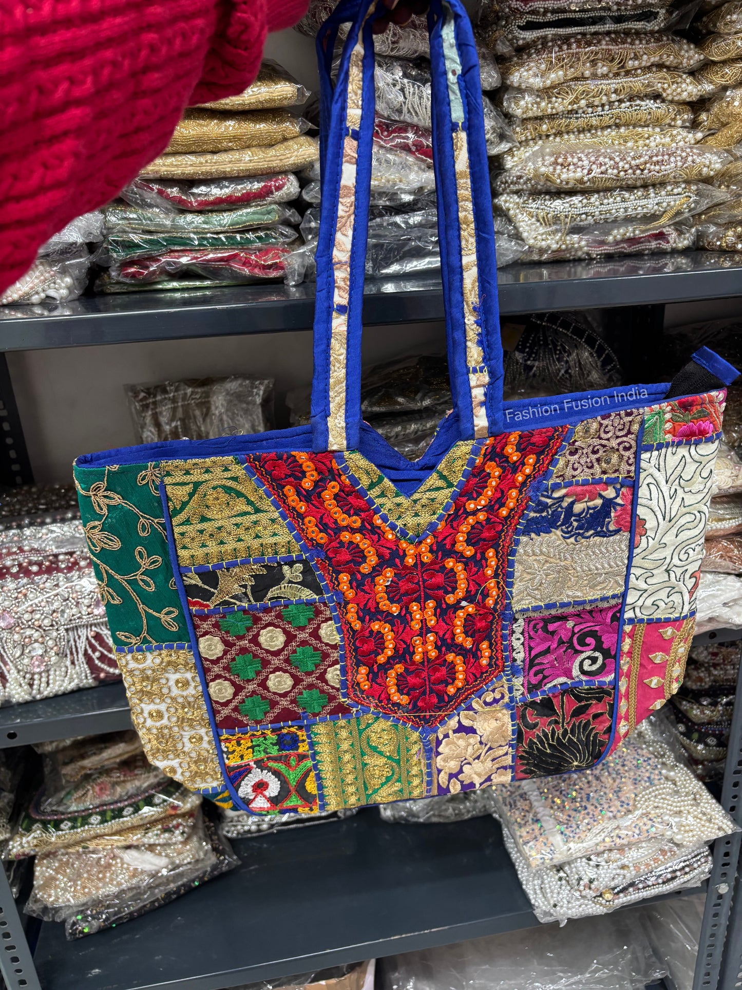 Colorful embroidered bag with blue handles on a shelf with other bags.