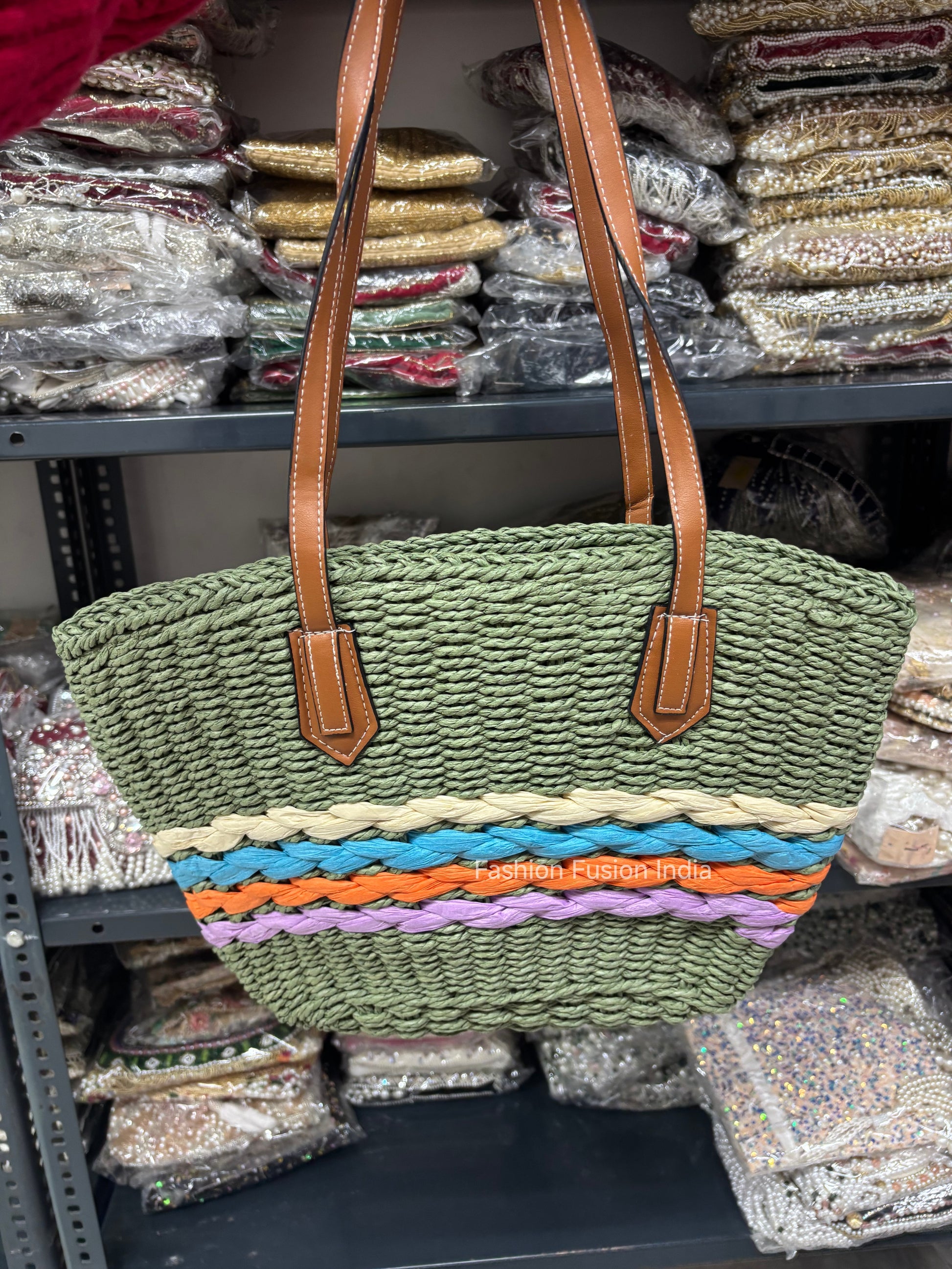 Green woven bag with brown straps on a shelf with fabric in the background