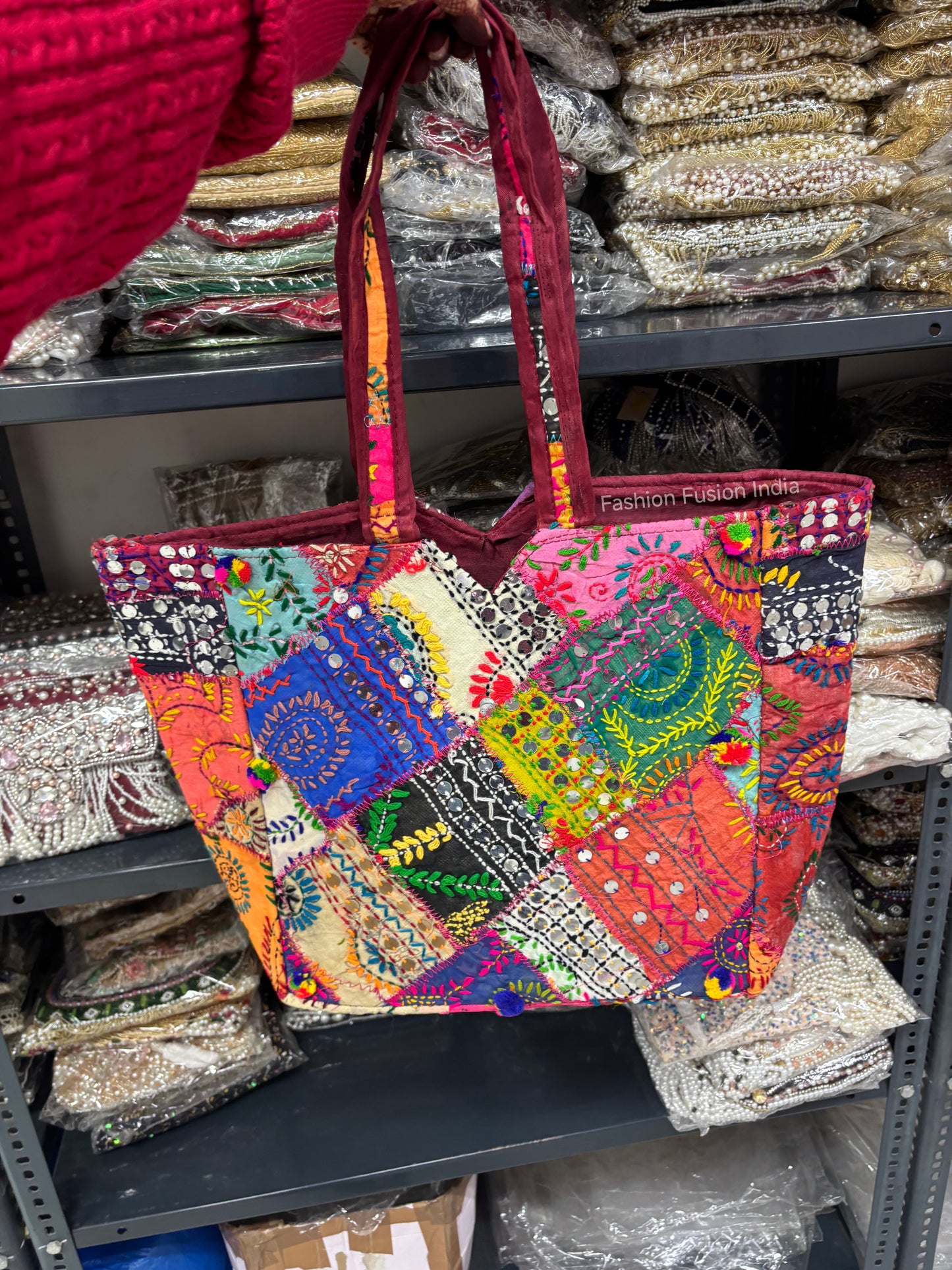 Colorful patchwork bag held by a person with shelves of fabric in the background