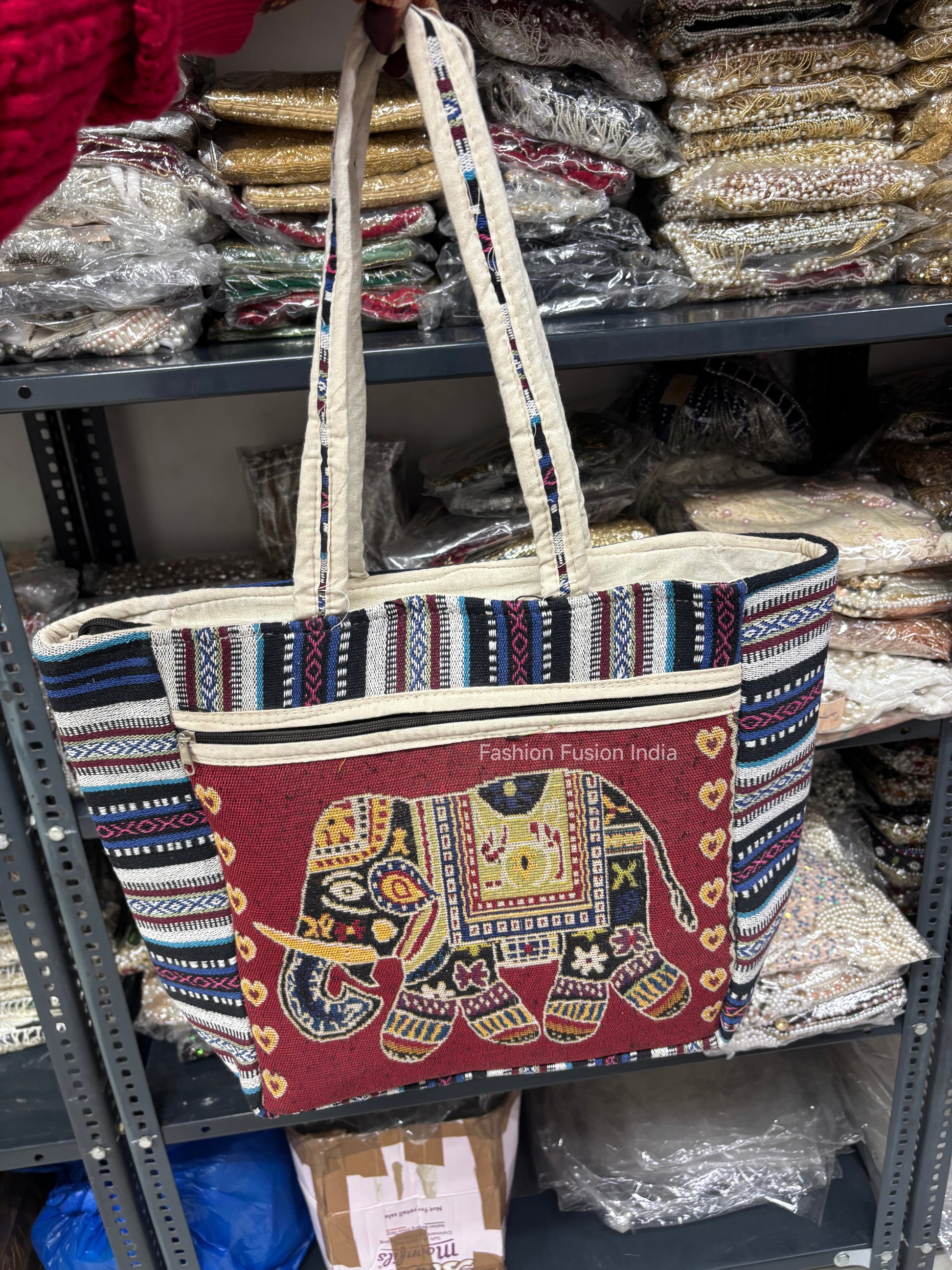 Tote bag with elephant design and 'Fashion Fusion India' text on a shelf with fabric items.