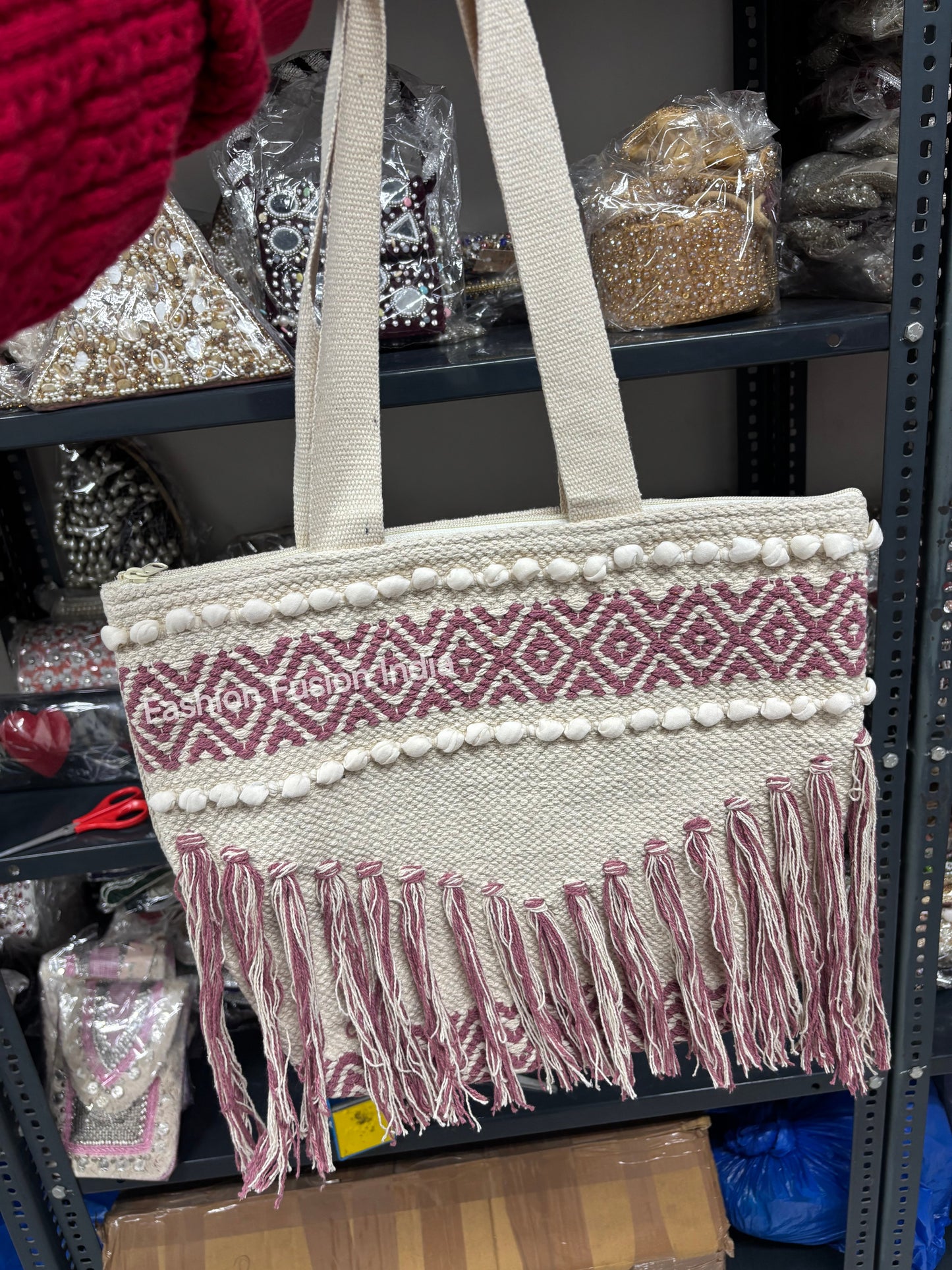 Beige tote bag with red pattern and fringe on a shelf