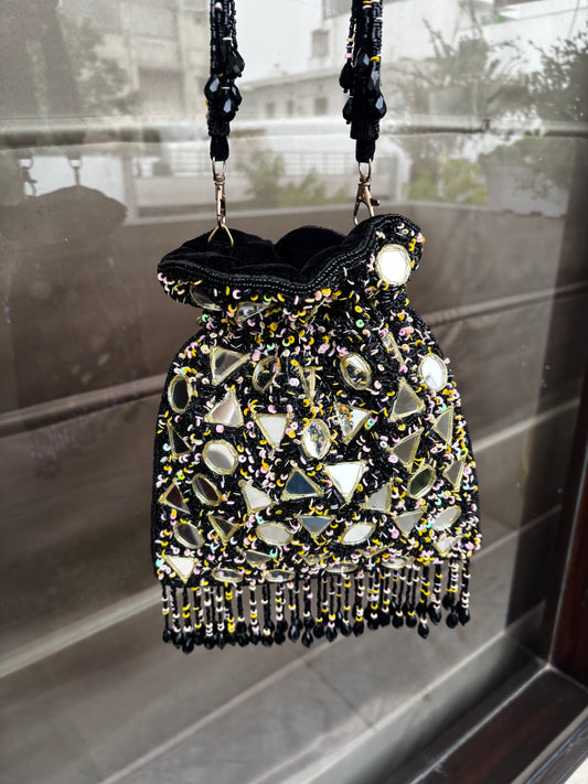 Beaded handbag with black strap on a reflective surface