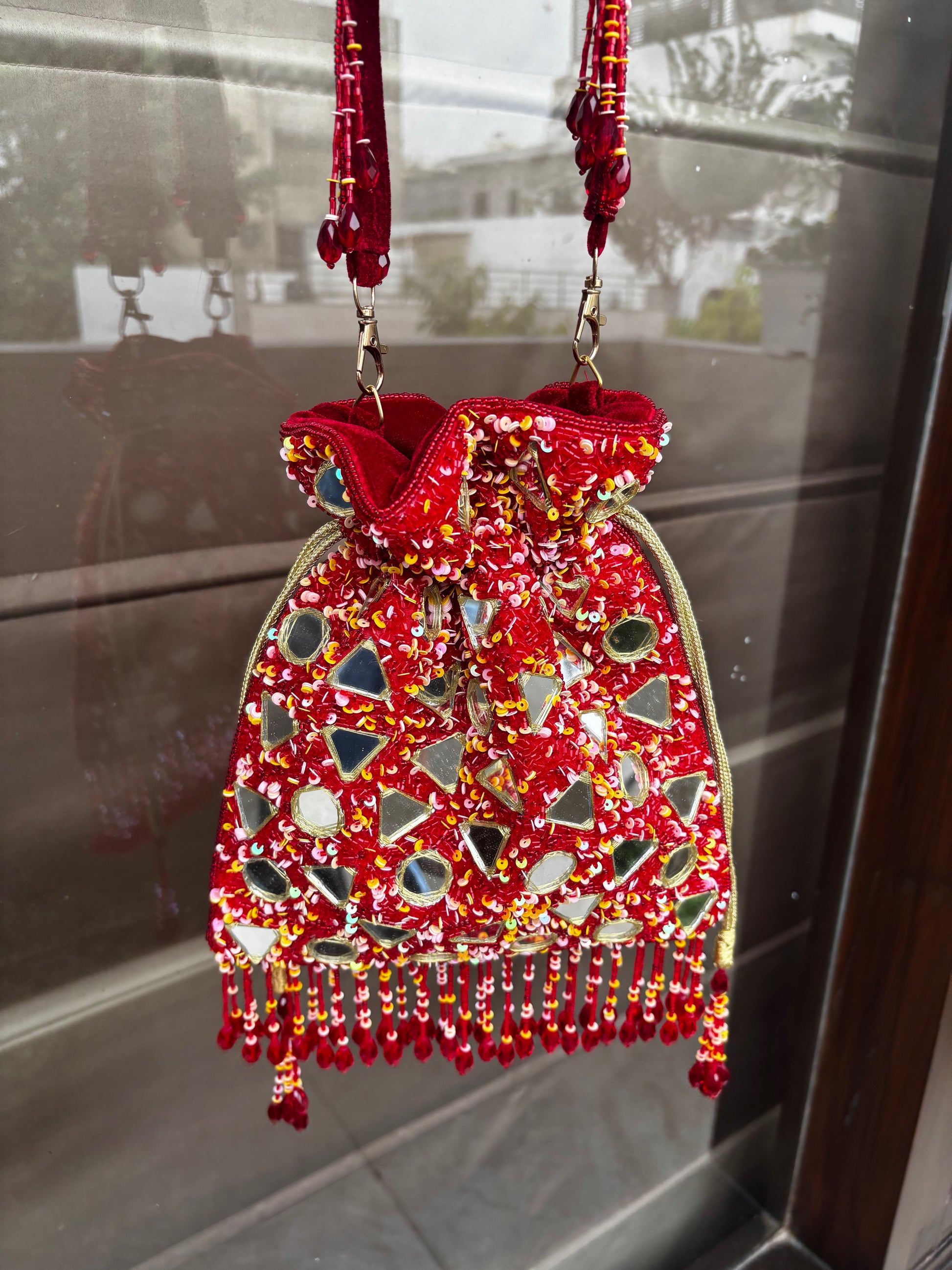 Decorative red bag with beaded details hanging on a reflective surface