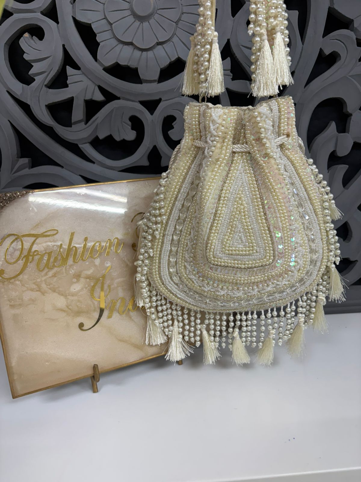 Decorative handbag with pearls and tassels on a white surface with a decorative background.