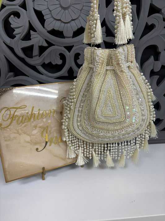 Decorative handbag with pearls and tassels on a white surface with a decorative background.