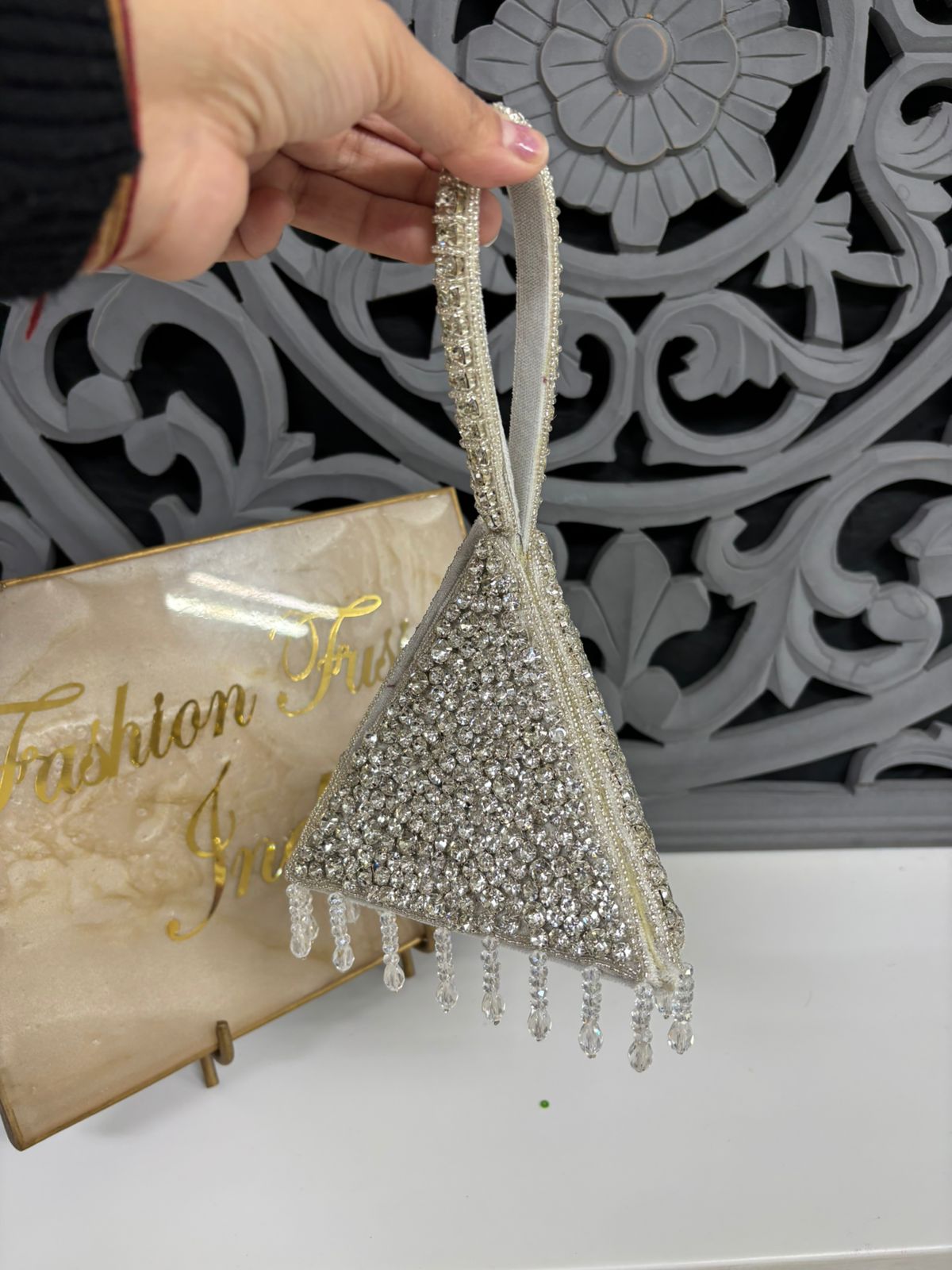 Decorative silver ornament with tassels held by a hand against a decorative wall.