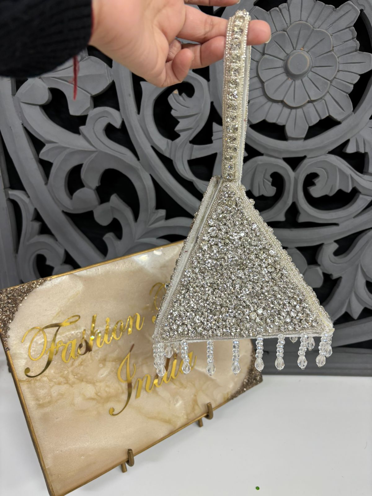 Decorative broom with crystal embellishments on a stand, against a decorative wall.