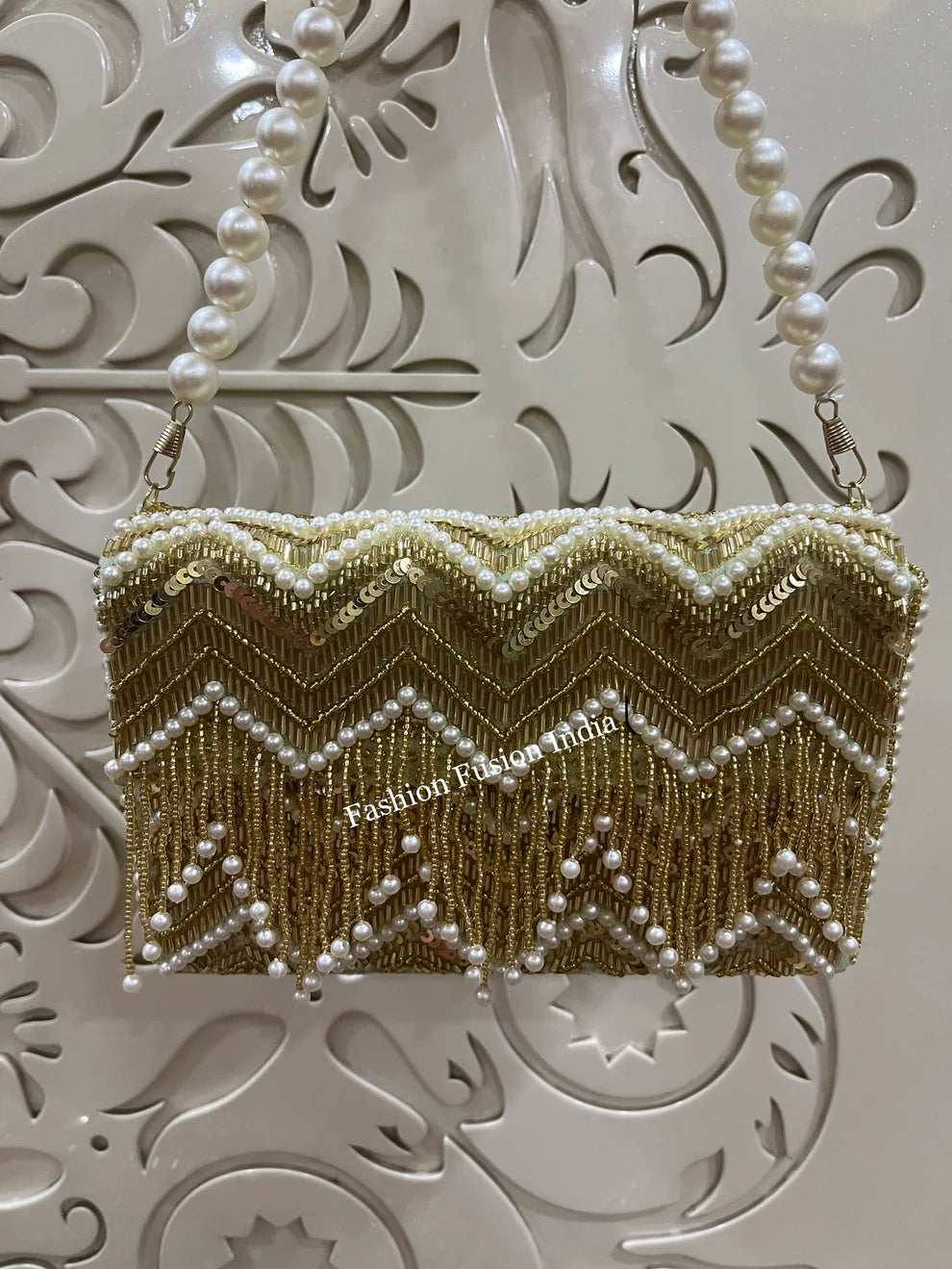 Gold beaded clutch with pearls on a decorative white background