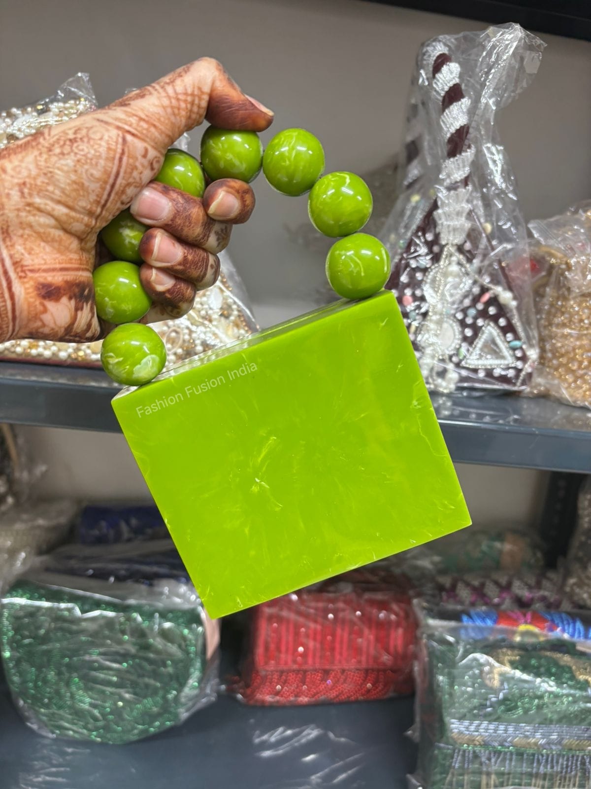 Hand holding a green block with 'Fashion Fusion India' branding, surrounded by plastic-wrapped items.