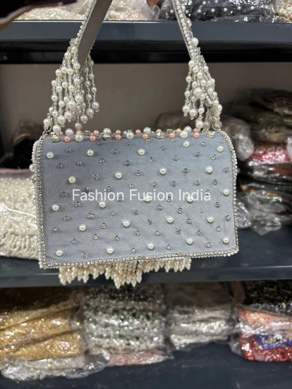 Decorative handbag with pearls and beads on a reflective surface, branded 'Fashion Fusion India'.