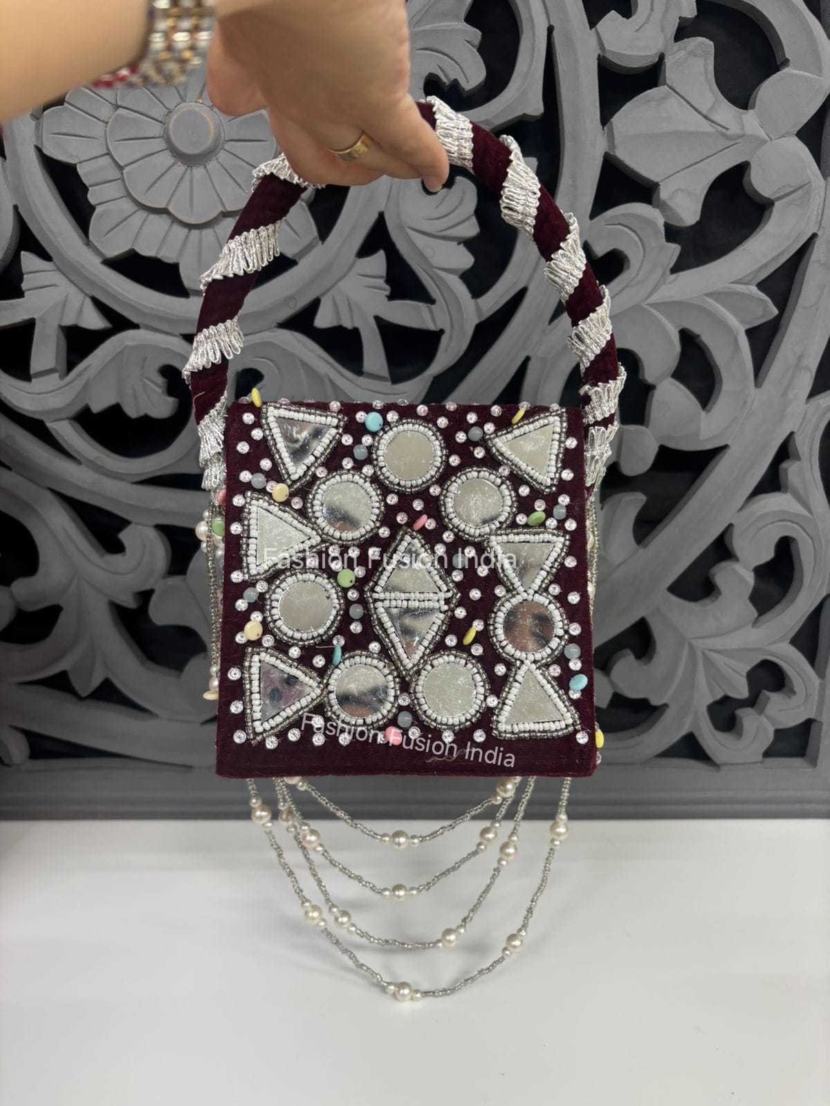 Handbag with decorative patterns and beads held by a hand against a decorative wall.
