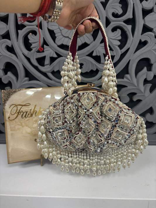 Decorative handbag with pearls and crystals held by a hand against a decorative background.