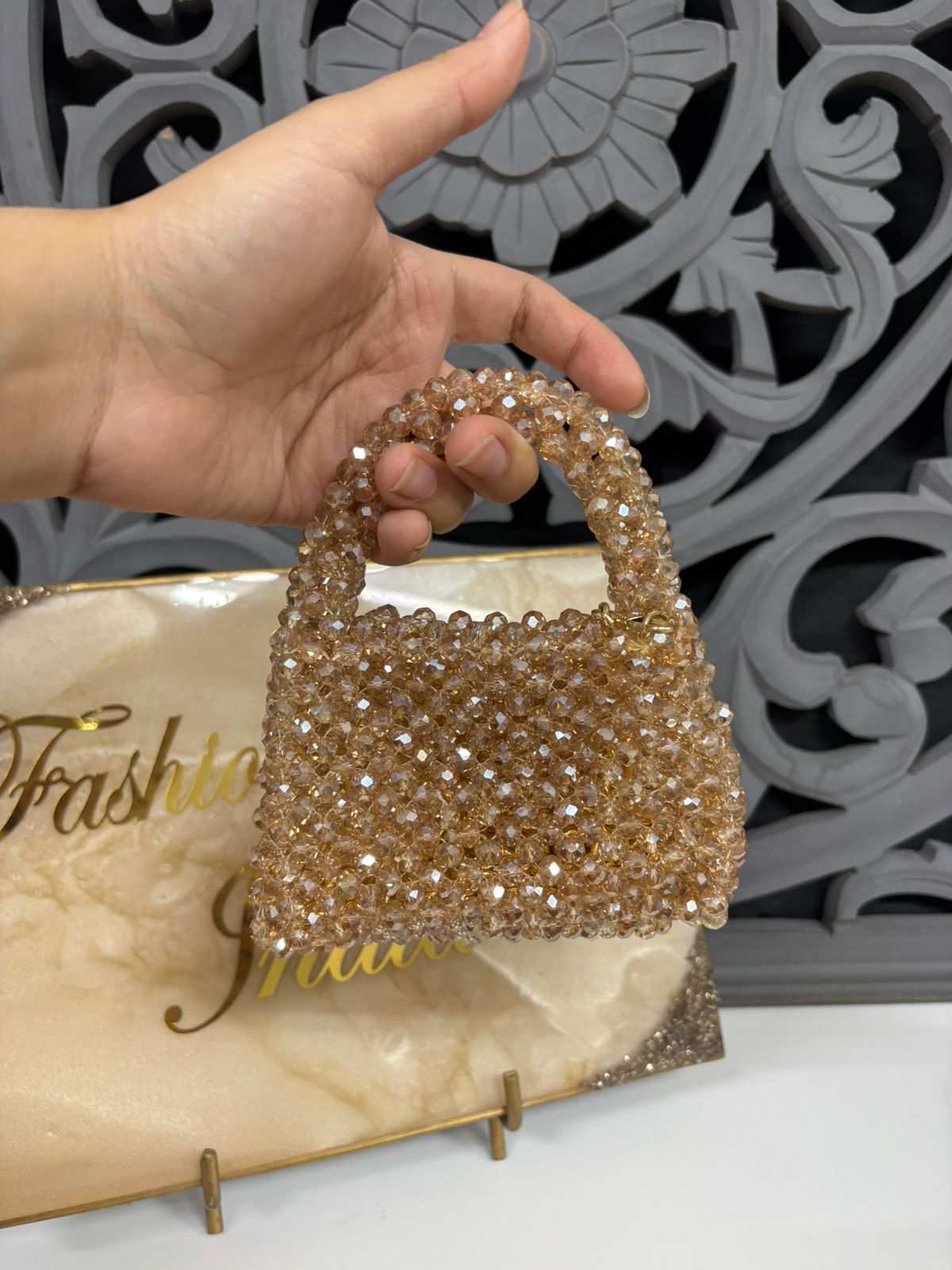 Gold beaded handbag held by a hand with a decorative background