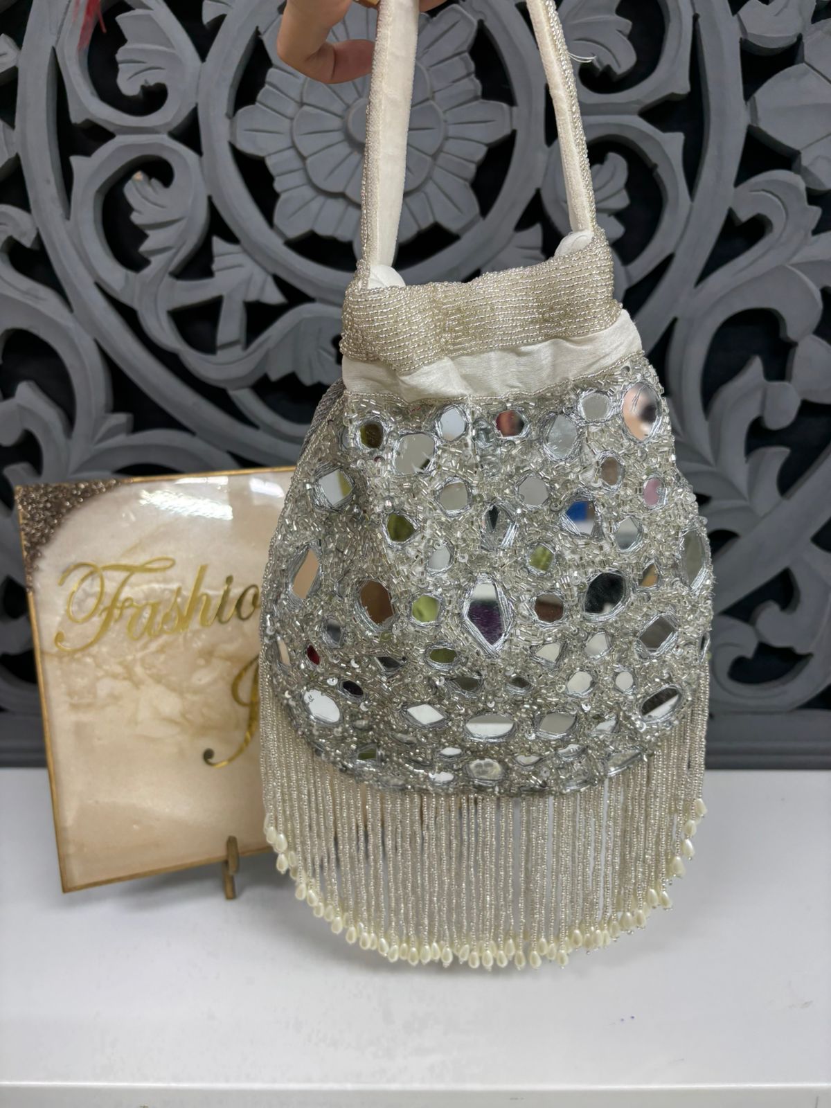 Decorative handbag with beads and fringes on a white surface with a decorative background.