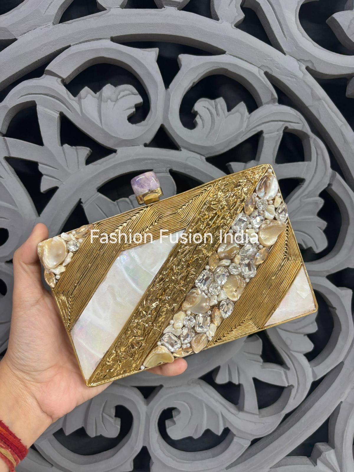 Gold and white decorative clutch held by a hand with a patterned background