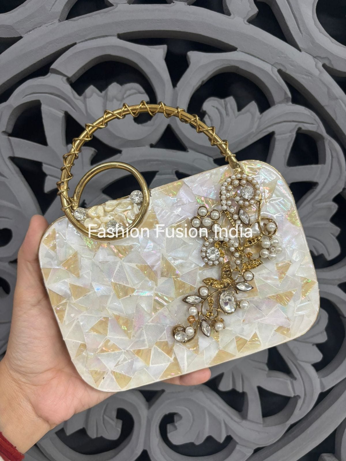 Decorative handbag with gold handle and embellishments held by a hand against a decorative background.