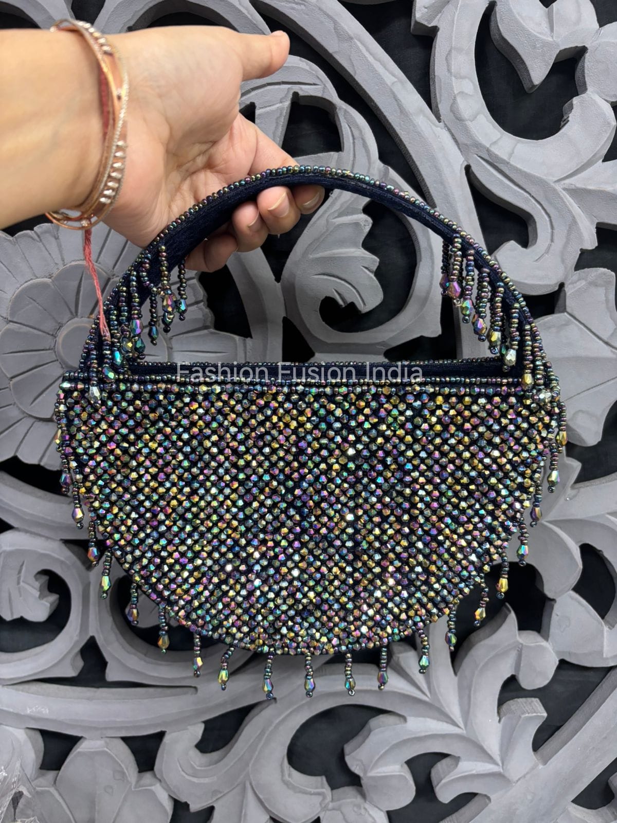 Handbag with beaded detailing held by a hand against an ornate decorative background.