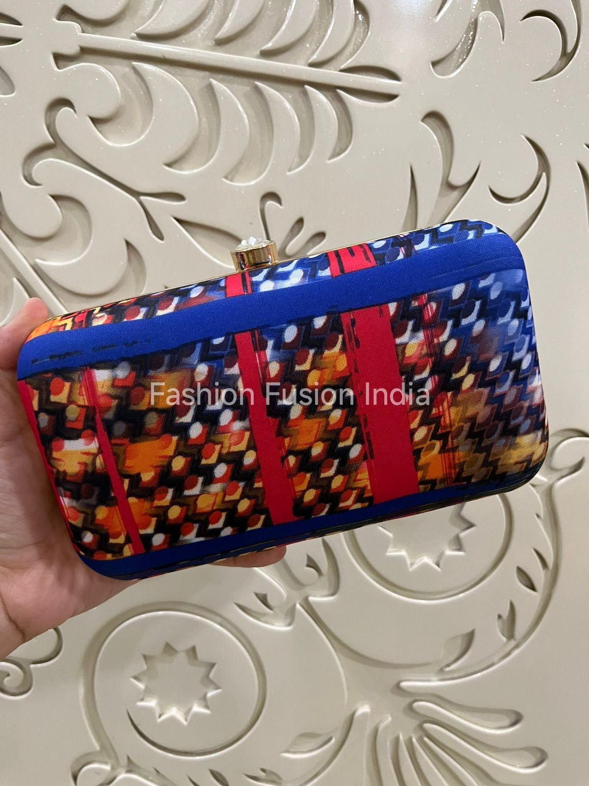 Colorful patterned clutch held by a hand against a decorative white background with 'Fashion Fusion India' branding.