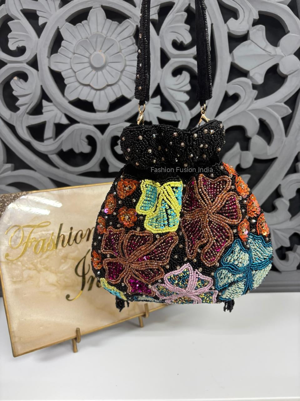 Decorative handbag with butterfly patterns on a stand against a decorative wall.