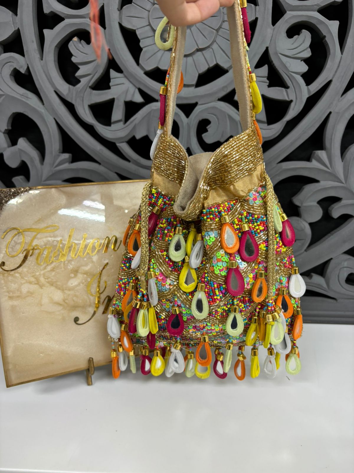 Decorative handbag with colorful beads and a 'Fashion' sign in the background