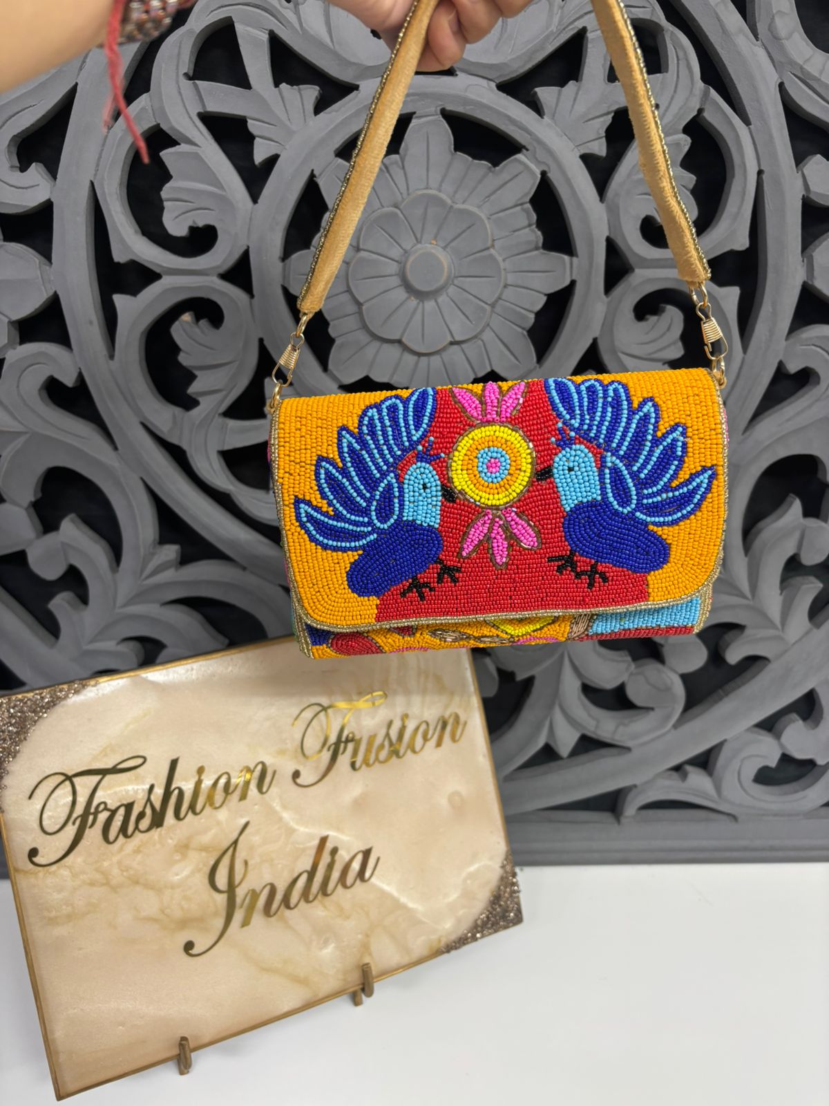 Colorful handbag with bird design held by a hand, placed on a decorative surface with 'Fashion Fusion India' sign.