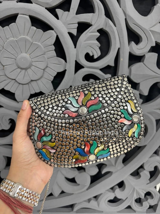 Decorative clutch with colorful floral patterns held by a hand against an ornate gray background.