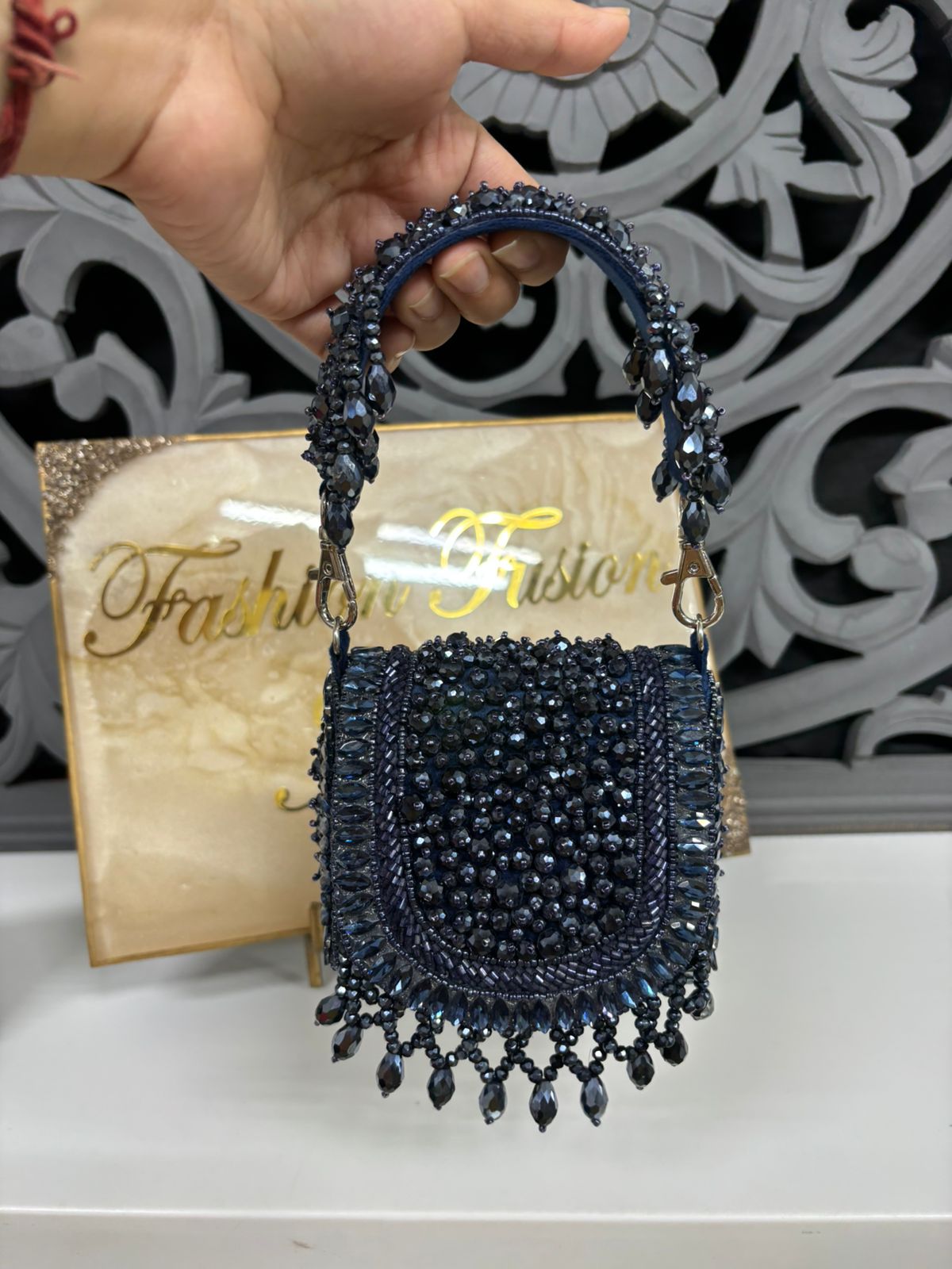 Navy blue beaded handbag held by a hand with a decorative background