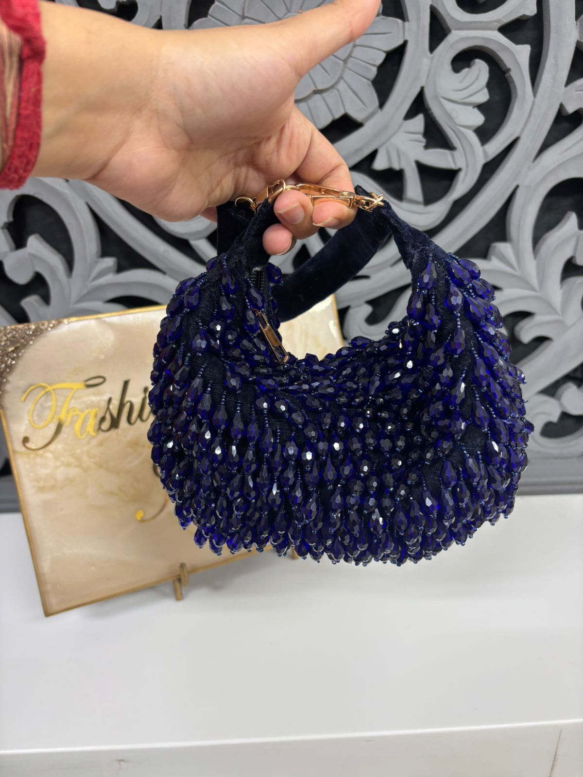 Hand holding a blue beaded handbag with a decorative background