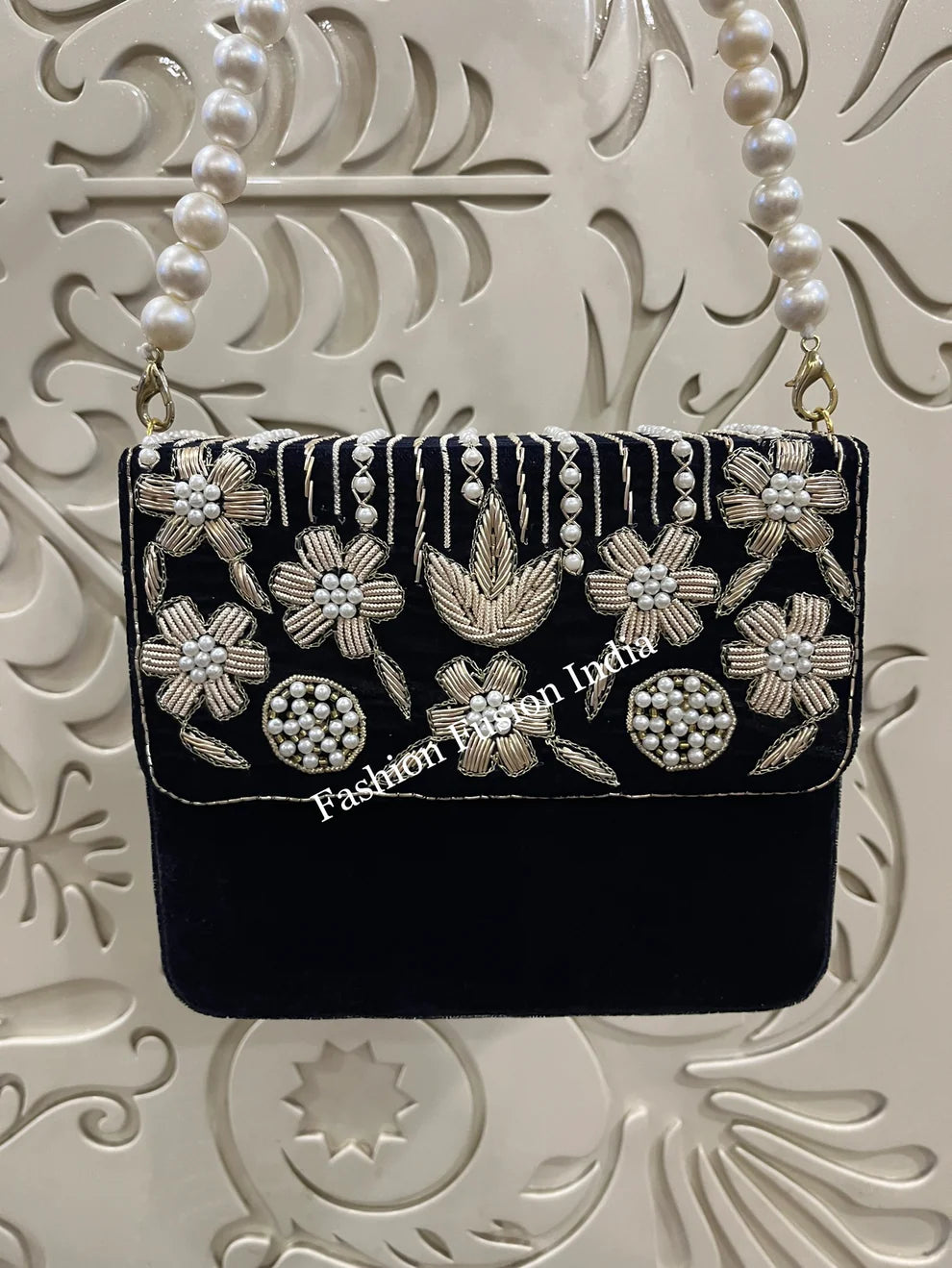 Navy blue handbag with floral embroidery and pearl details on a decorative white background