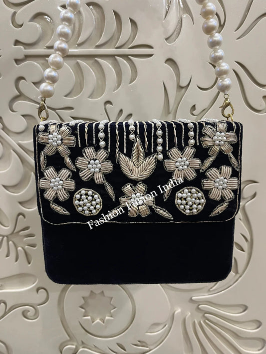 Navy blue handbag with floral embroidery and pearl details on a decorative white background